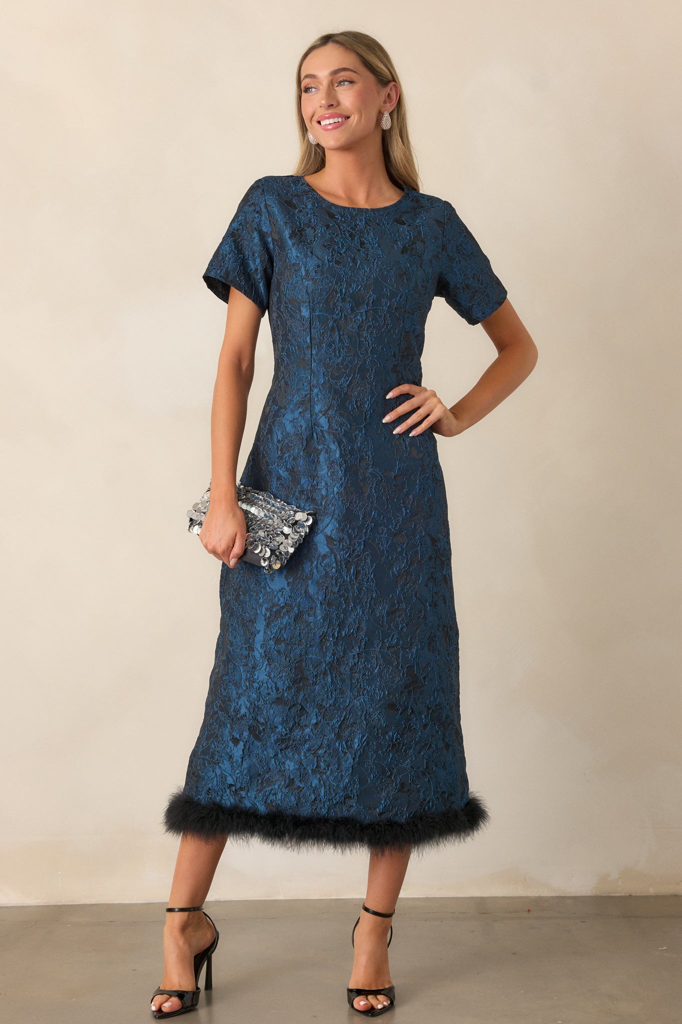 Angled view of the dress showing the structured design, emphasizing the smooth fabric, short sleeves, and the unique faux fur detail at the bottom hem.