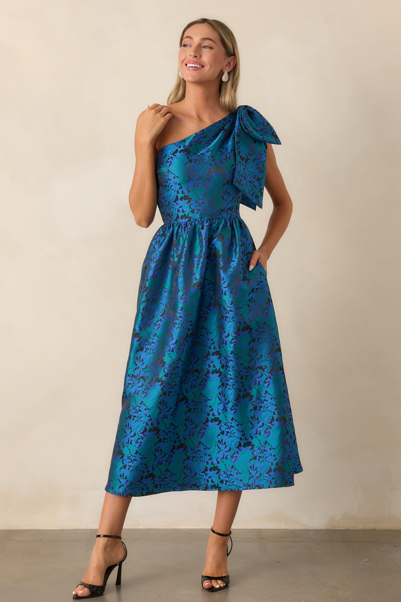 Another front view of the blue midi dress, highlighting the elegant draping of the jacquard fabric, one-shoulder design, and the flare of the skirt.