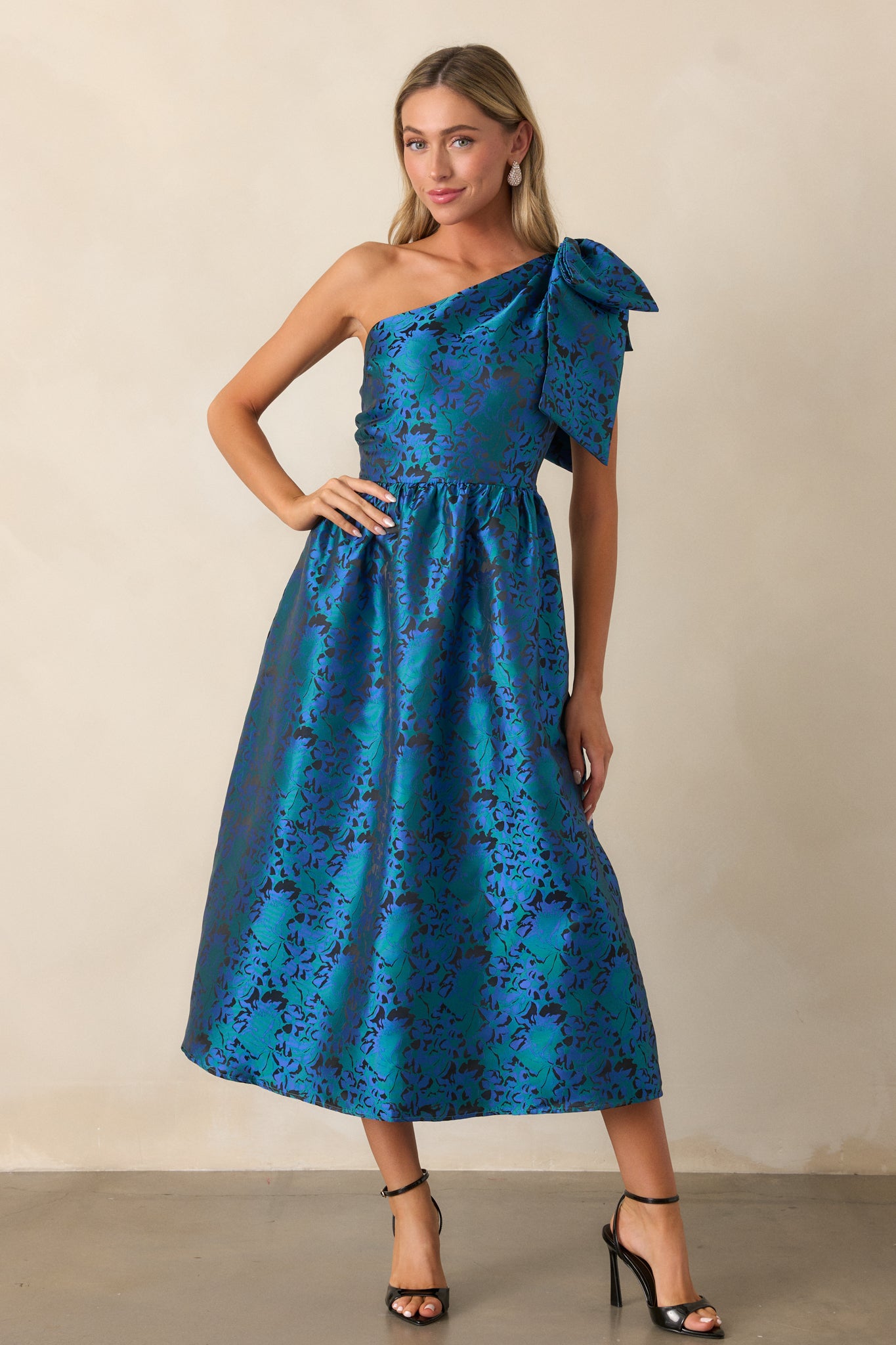 Full-body view of the blue midi dress, showcasing the one-shoulder neckline with the bow embellishment and the flared skirt that creates a flattering fit and flare shape.