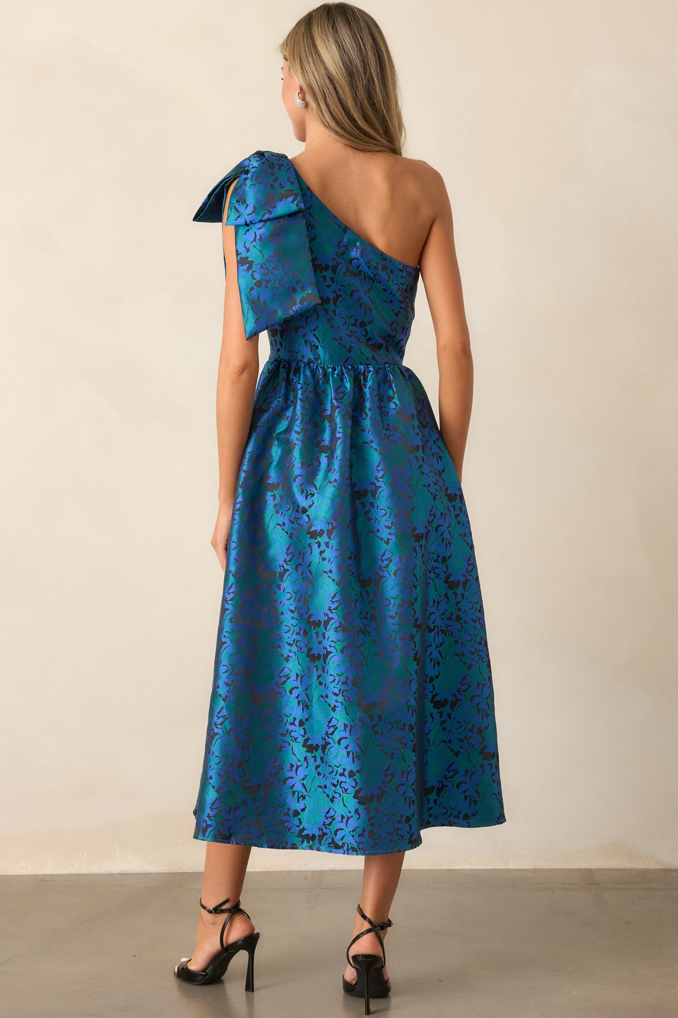 Back view of the blue midi dress, featuring the discrete back zipper, the smooth fit of the bodice, and the flow of the skirt, with the large bow detail clearly visible from the back.