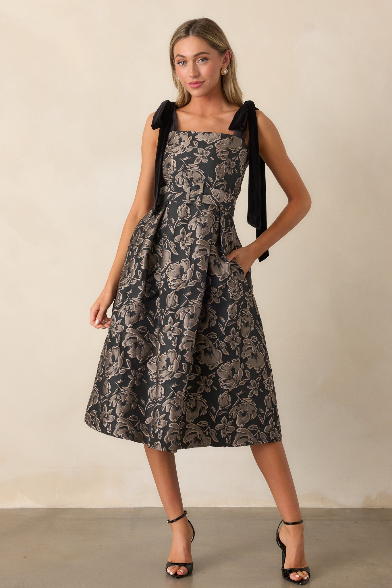 A front view of the black dress showcasing the square neckline, jacquard fabric, and self-tie velvet bow shoulder straps.