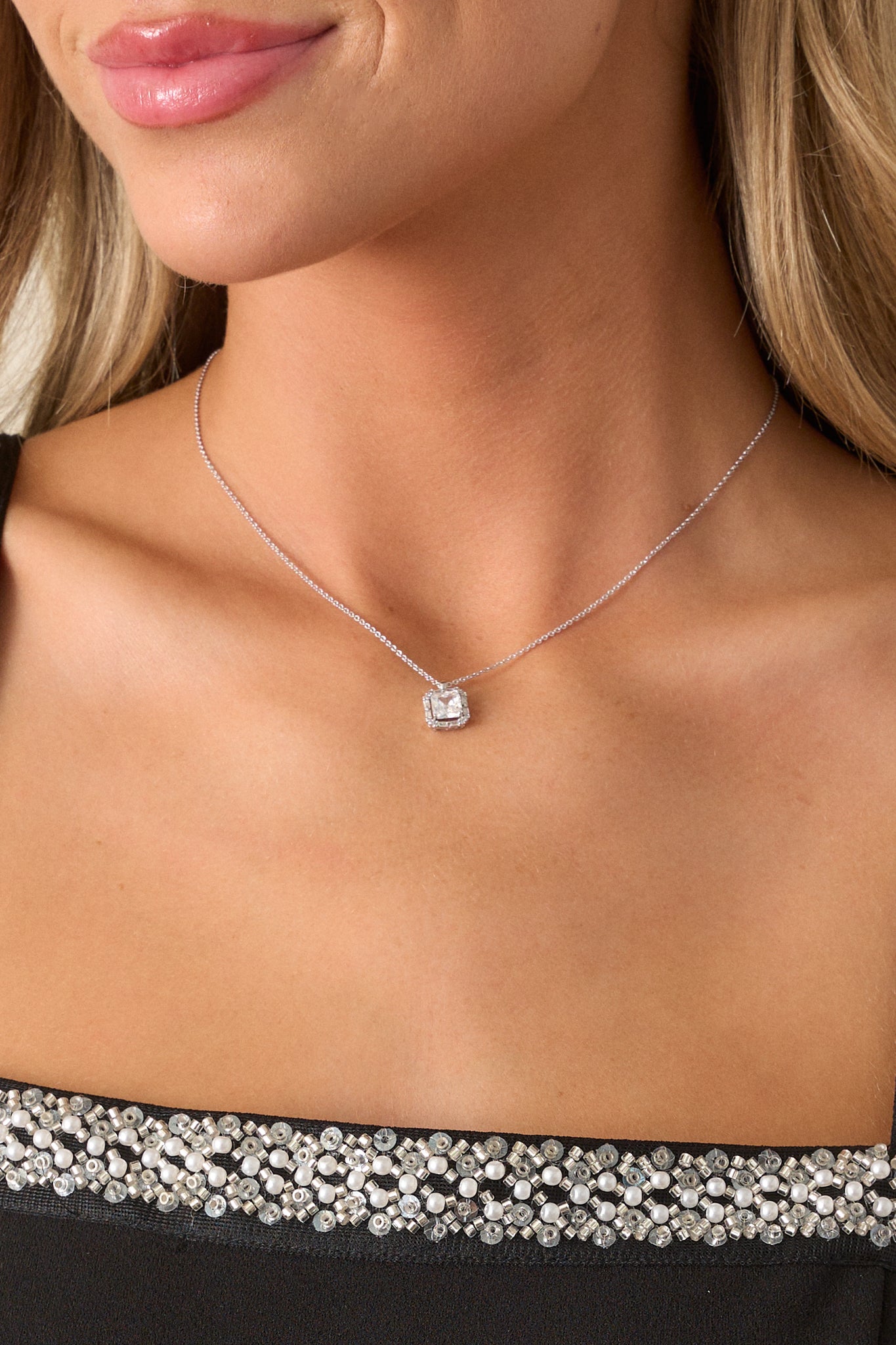 Focused shot of the silver necklace showcasing the small square pendant with a prominent rhinestone center, highlighting the delicate silver chain.