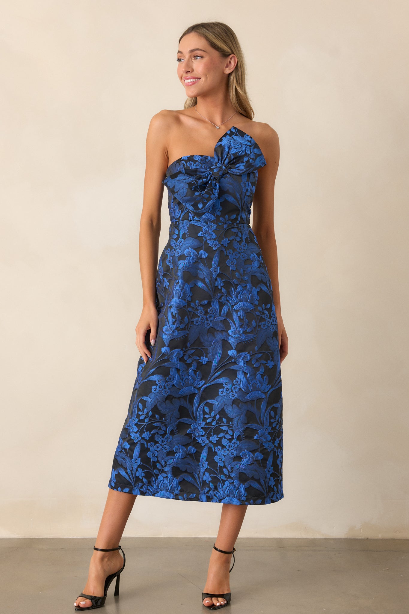 A front view of the midnight blue midi dress featuring a strapless neckline with a large bow embellishment, a structured design, and jacquard fabric.