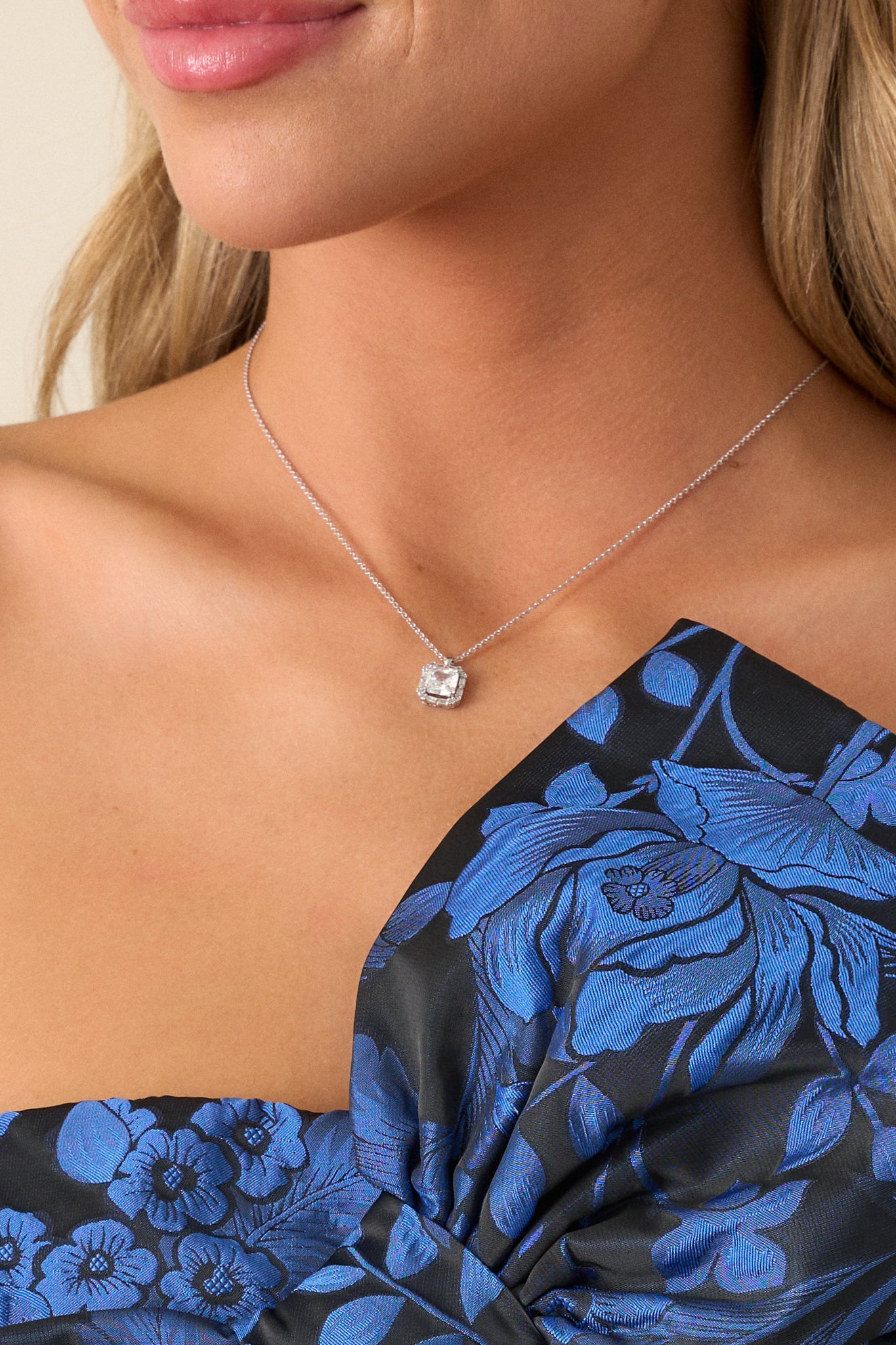 Close-up view of the silver necklace, featuring a thin silver chain and a small square pendant with a large square rhinestone center, sparkling in the light.