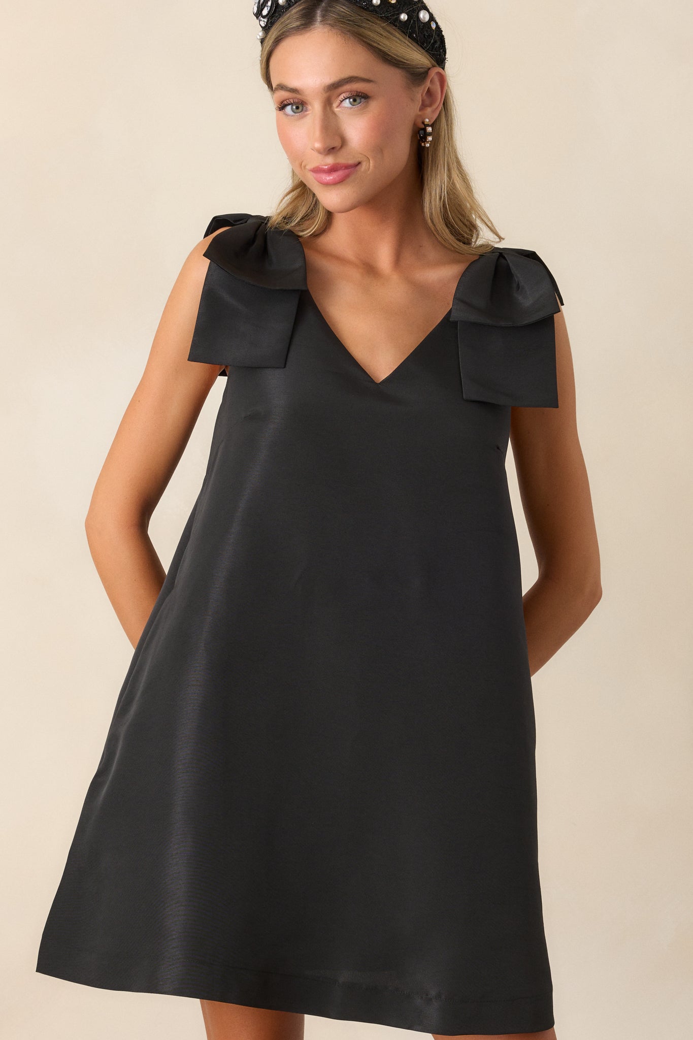 Front-facing shot of the black mini dress, focusing on the v-neckline, the elegant shift design, and the cute bows on the shoulders.