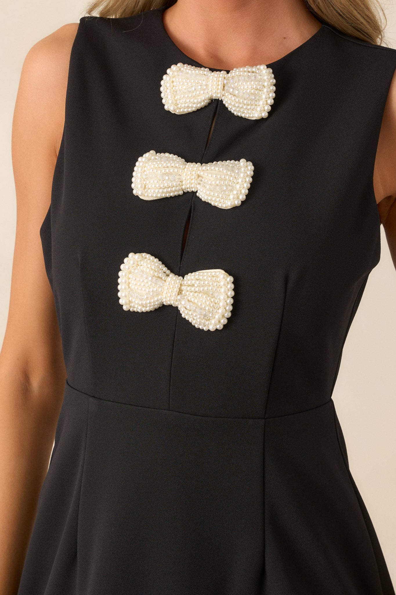 Close-up of the pearl-embellished bows on the black dress, showing the delicate detailing and how it contrasts with the sleek, structured fabric of the dress.