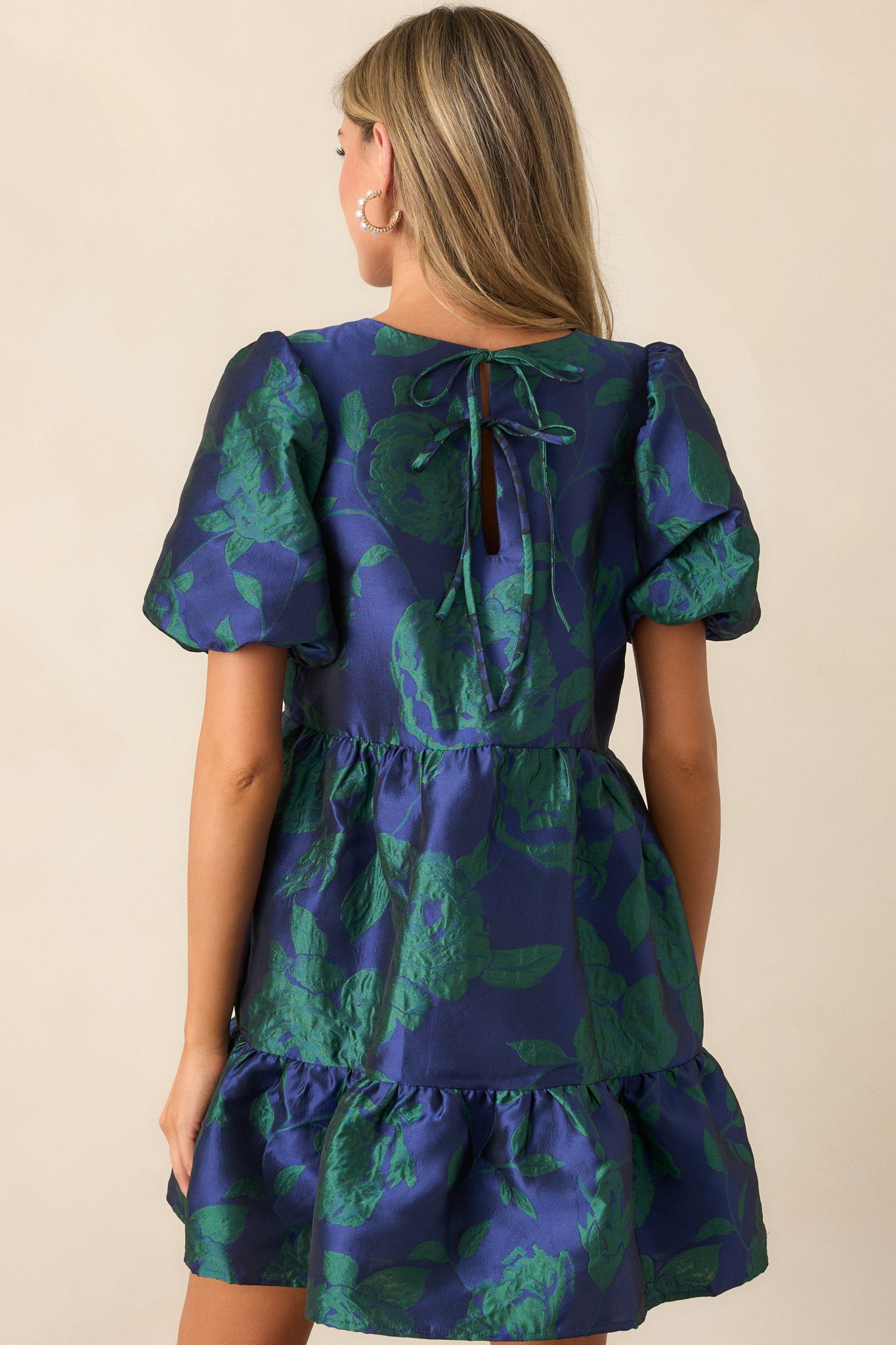 Back view of the midnight blue mini dress, displaying the keyhole closure with two self-tie bows and the textured jacquard fabric along the tiered skirt.