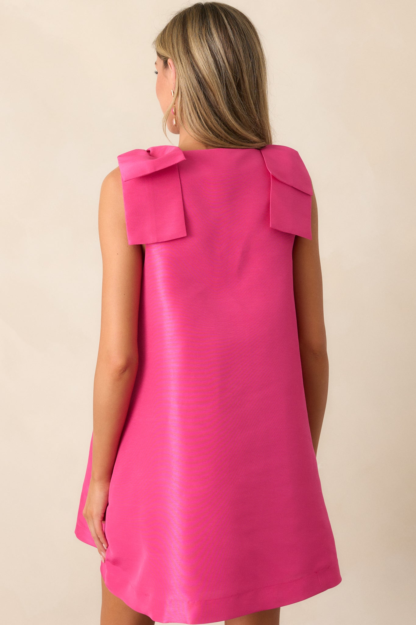 Back view of the fuchsia mini dress, capturing the relaxed fit, the minimalistic design, and the bows tied on both shoulders as a key feature.