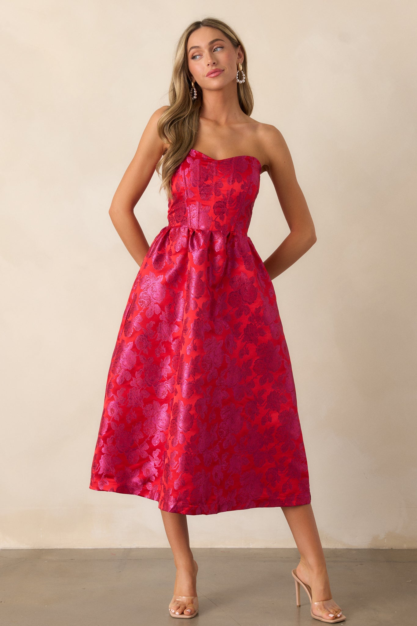 A complete shot of the red and pink midi dress showcasing the strapless sweetheart neckline and floral jacquard fabric, with structured boning visible in the front bodice.