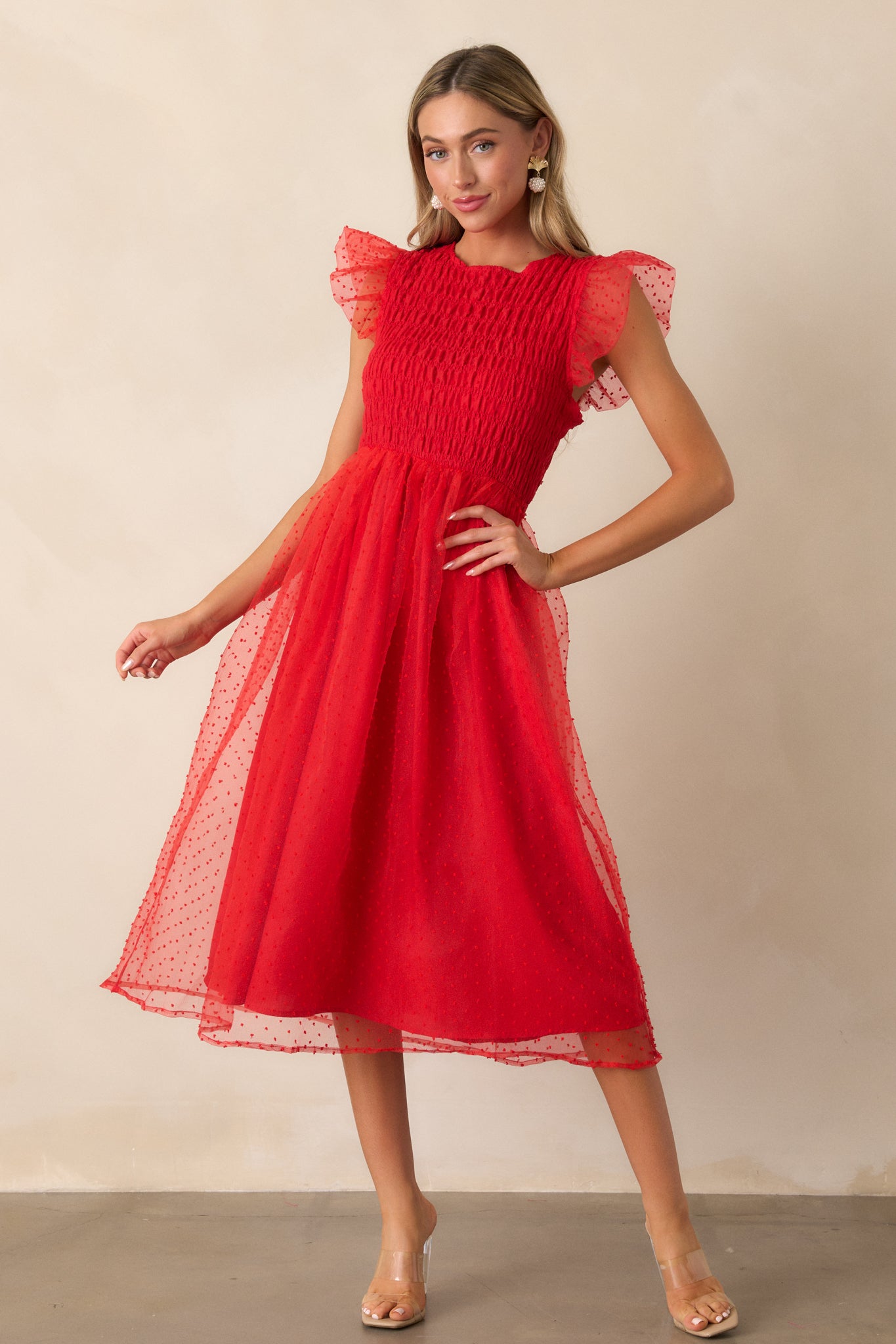 Angled shot showing the red dress with the rounded neckline and the sheer, whimsical polka dot tulle overlay extending gracefully over the bodice and skirt.