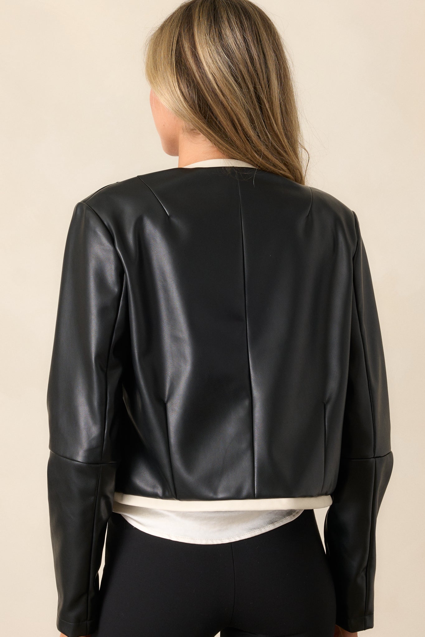 A back view of the black jacket highlighting its cropped length, clean design, and the ivory faux leather trim running along the edges.