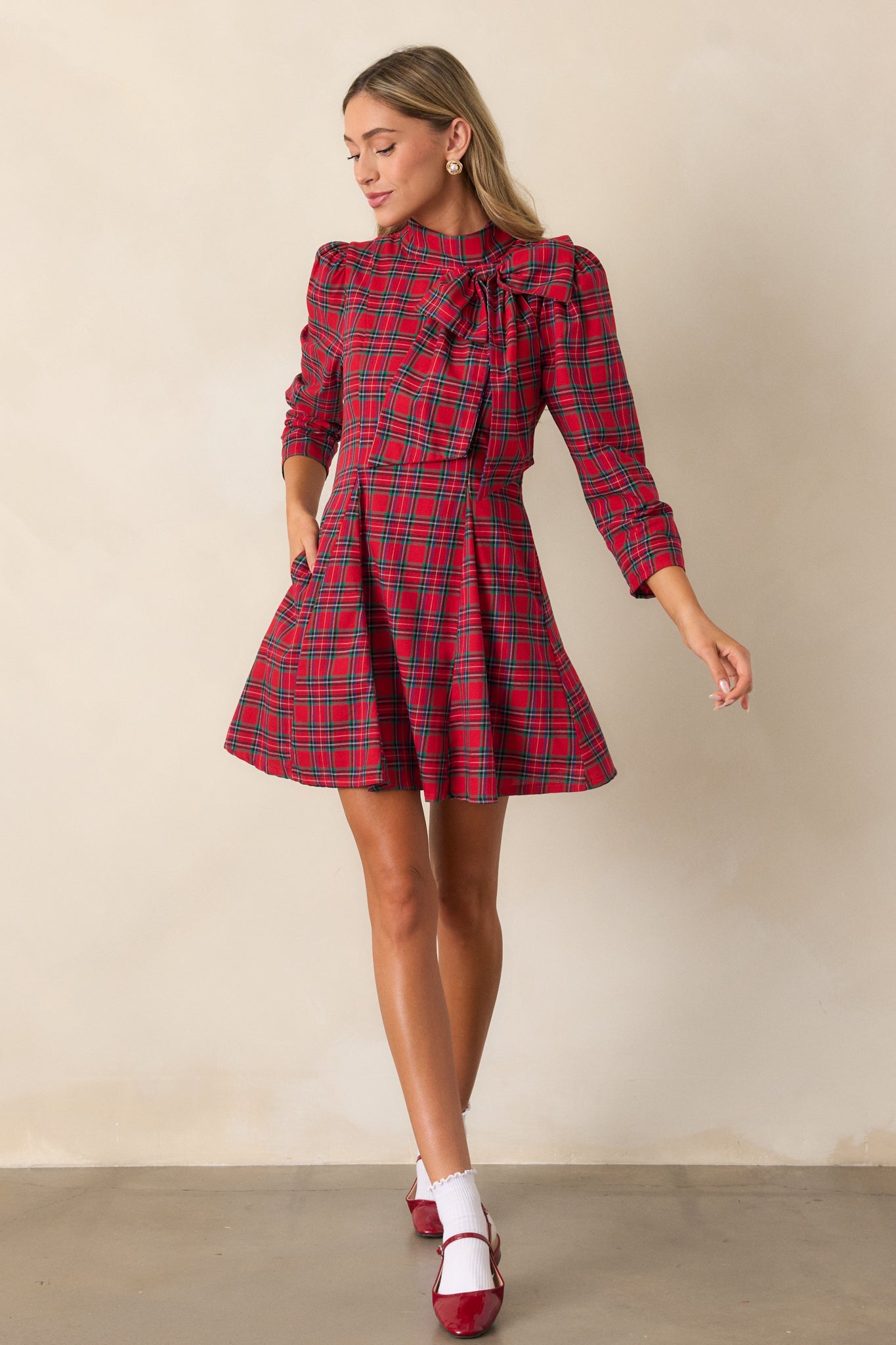 A red mini dress with a high neckline adorned with a bow detail, featuring a fit and flare silhouette and a plaid pattern, shown from the front.