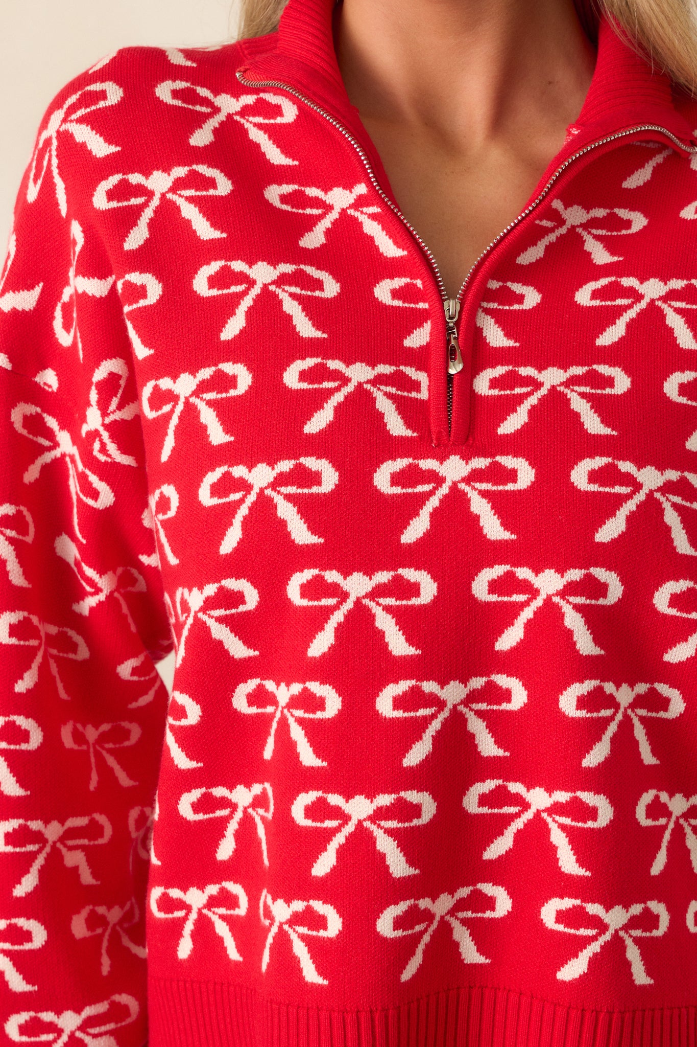 A detailed close-up of the ivory bow print across the fabric, showcasing the quality and placement of the pattern, as well as the smooth texture of the red pullover.