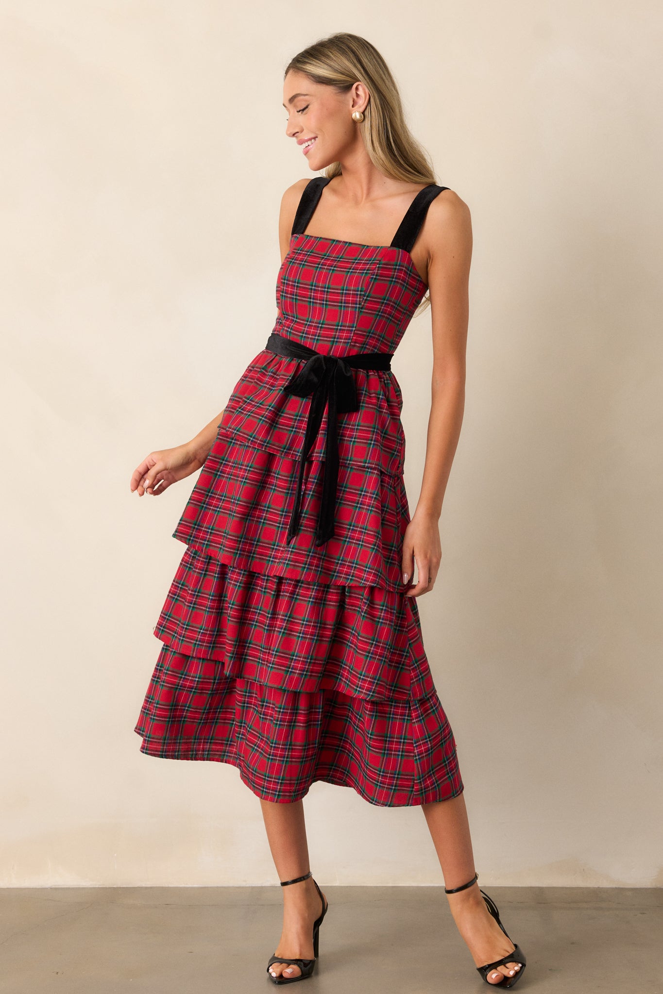 Three-quarter angle view of the red dress, showing the plaid print and the subtle volume from the tiered skirt, with velvet shoulder straps adding texture.