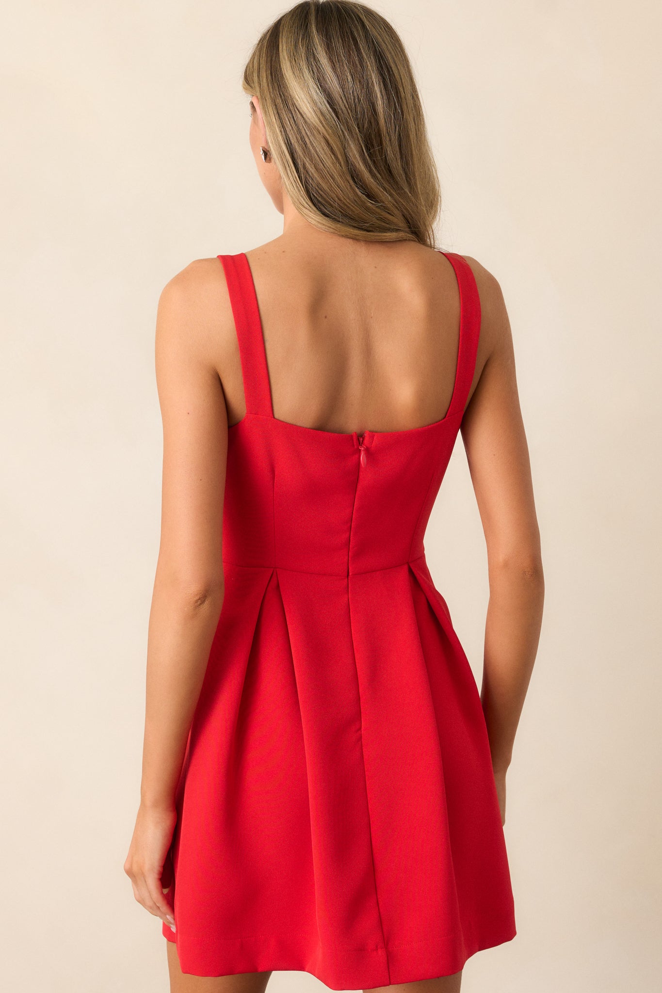 Back view of the red dress, focusing on the clean lines of the sleeveless design, the pleated skirt, and the back silhouette of the square neckline.