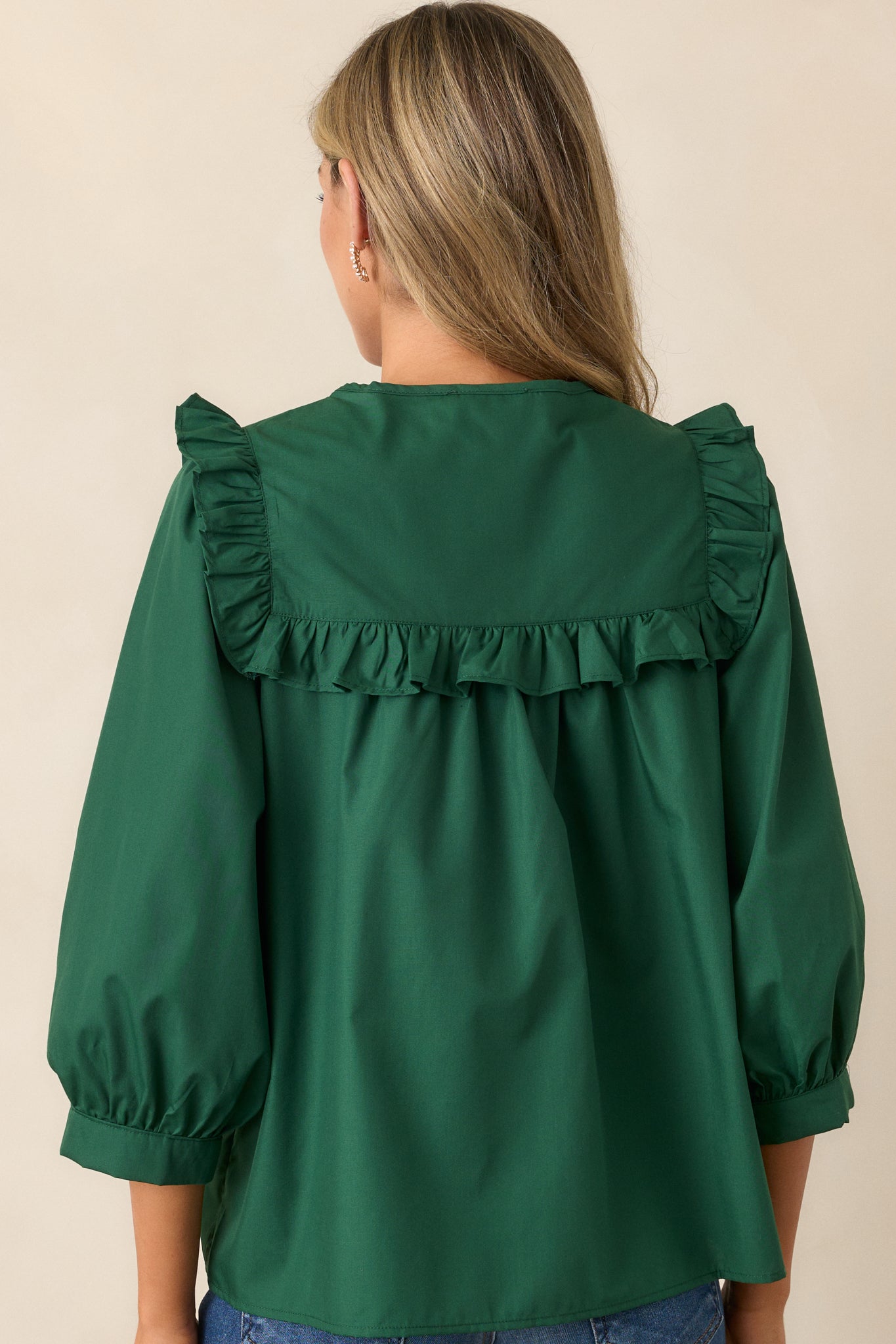 Back view of the hunter green top, featuring the smooth back and the continuation of the faux pearl lattice yoke with ruffle detailing, highlighting the elegant fit.