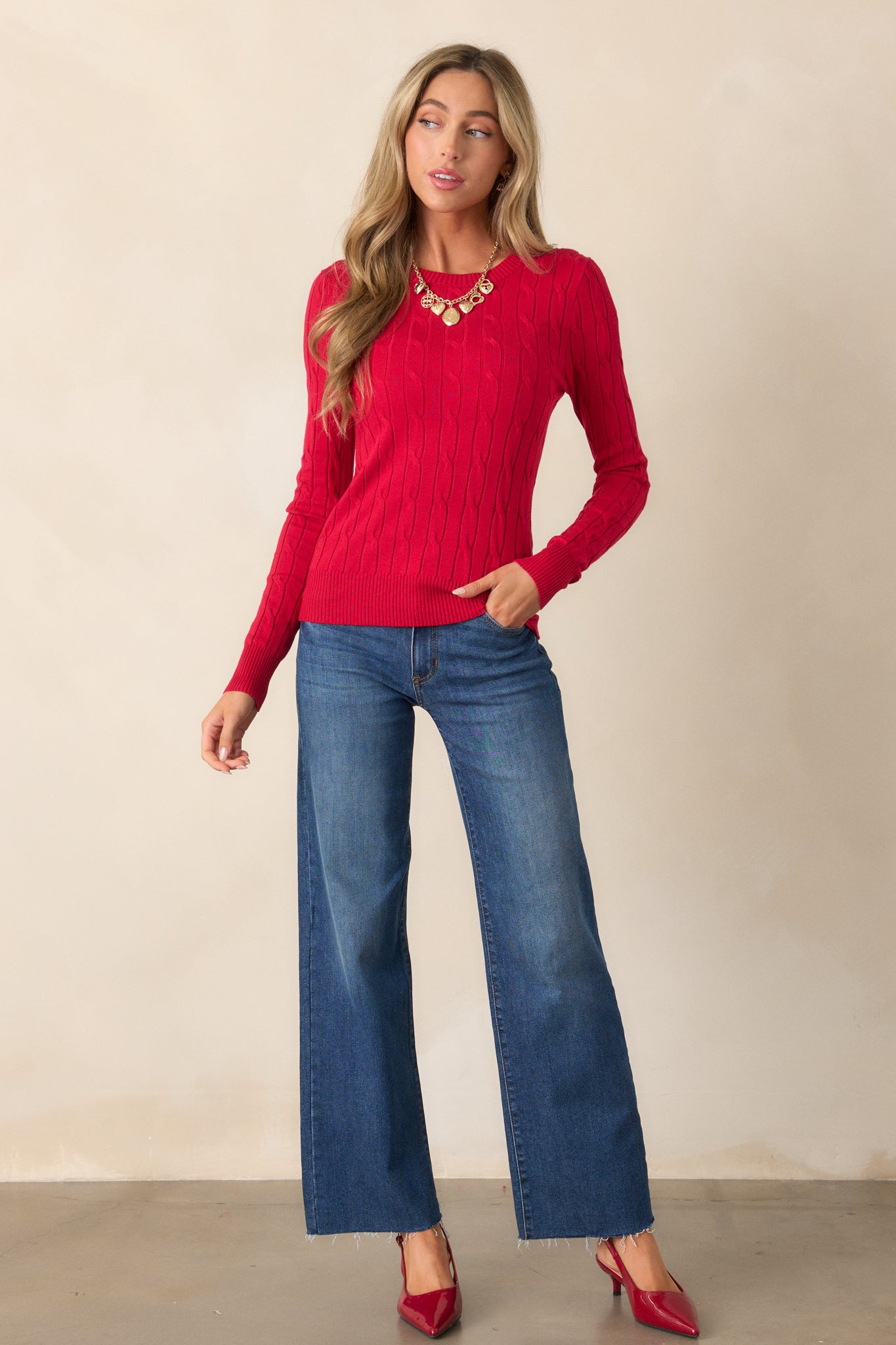 A full-length image focusing on the bold red sweater's intricate cable knit texture and classic fit.