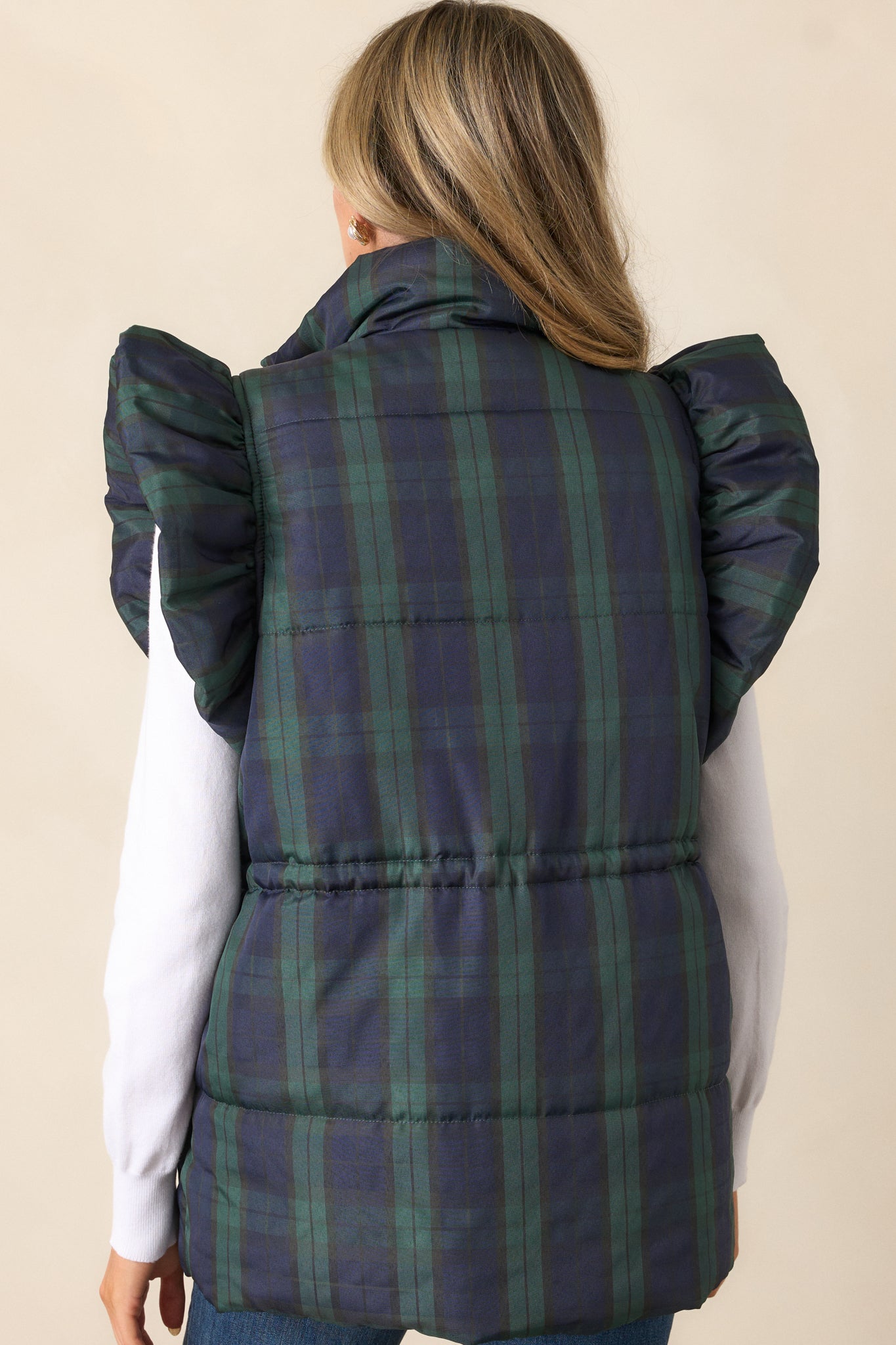 Full back view of the navy puffer vest, emphasizing the plaid pattern, puffer line detailing, and cinched waist design.