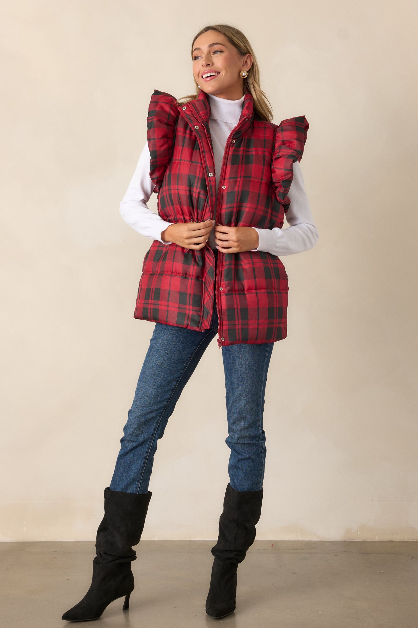 A front view of the red puffer vest emphasizing the functional snap button and zipper closures and the drawstring cinch waist with silver hardware.