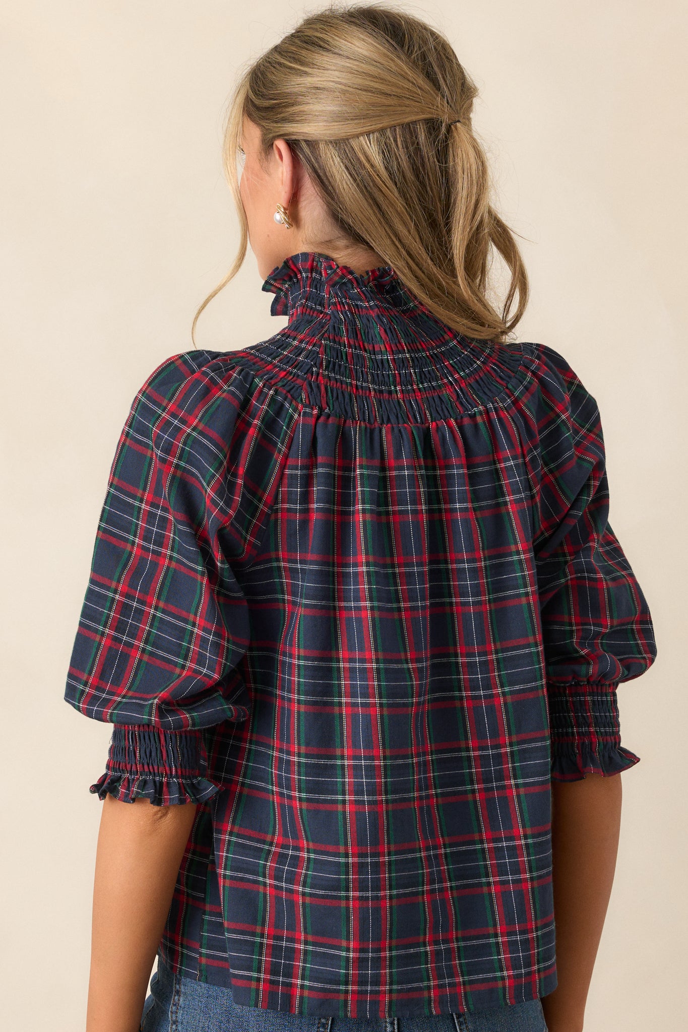 Back view of the navy blouse, showing the relaxed fit, puff sleeves, and the smooth flow of the plaid print across the back, with the high smocked neck completing the design.