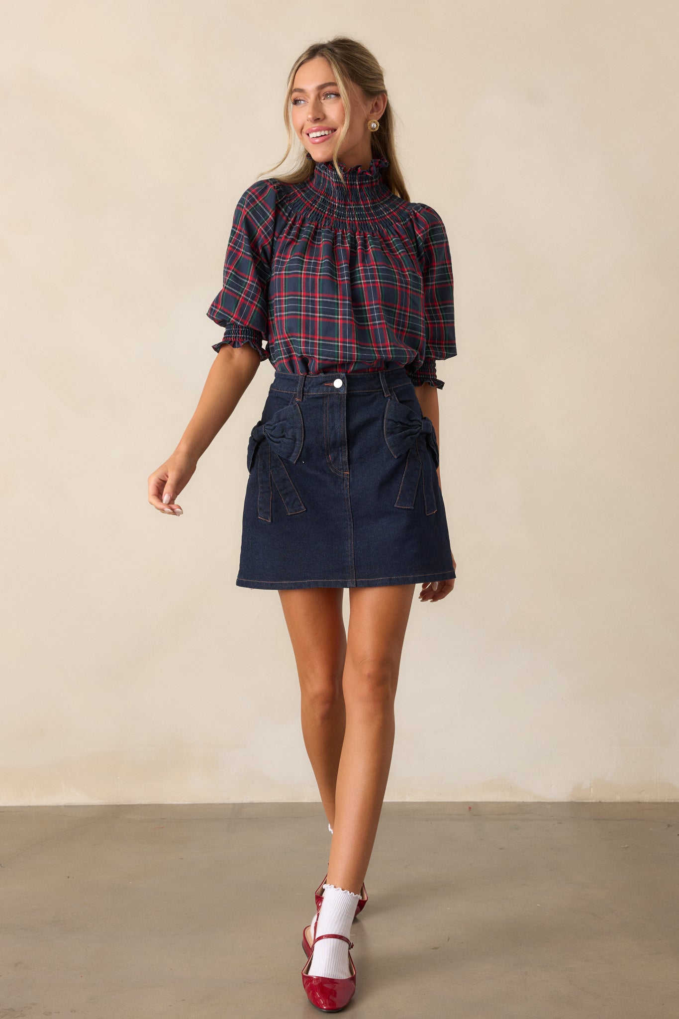 A full-length view of the navy blouse featuring a high smocked neck, puff sleeves, and smocked cuffs, with the relaxed fit and beautiful plaid print visible across the fabric.