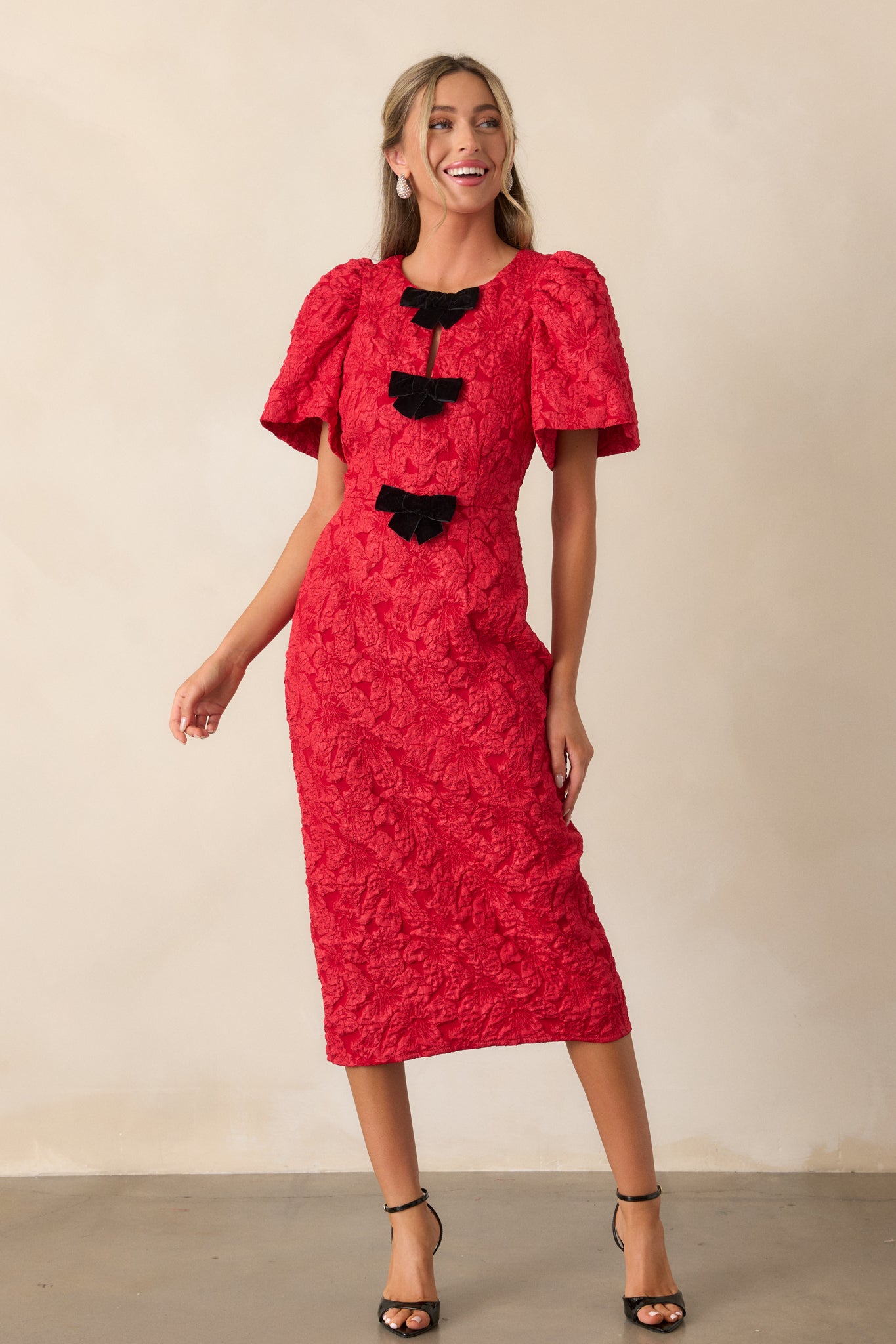 A front view of the red midi dress highlighting the round neckline, jacquard fabric, and three velvet bow details on the bodice.