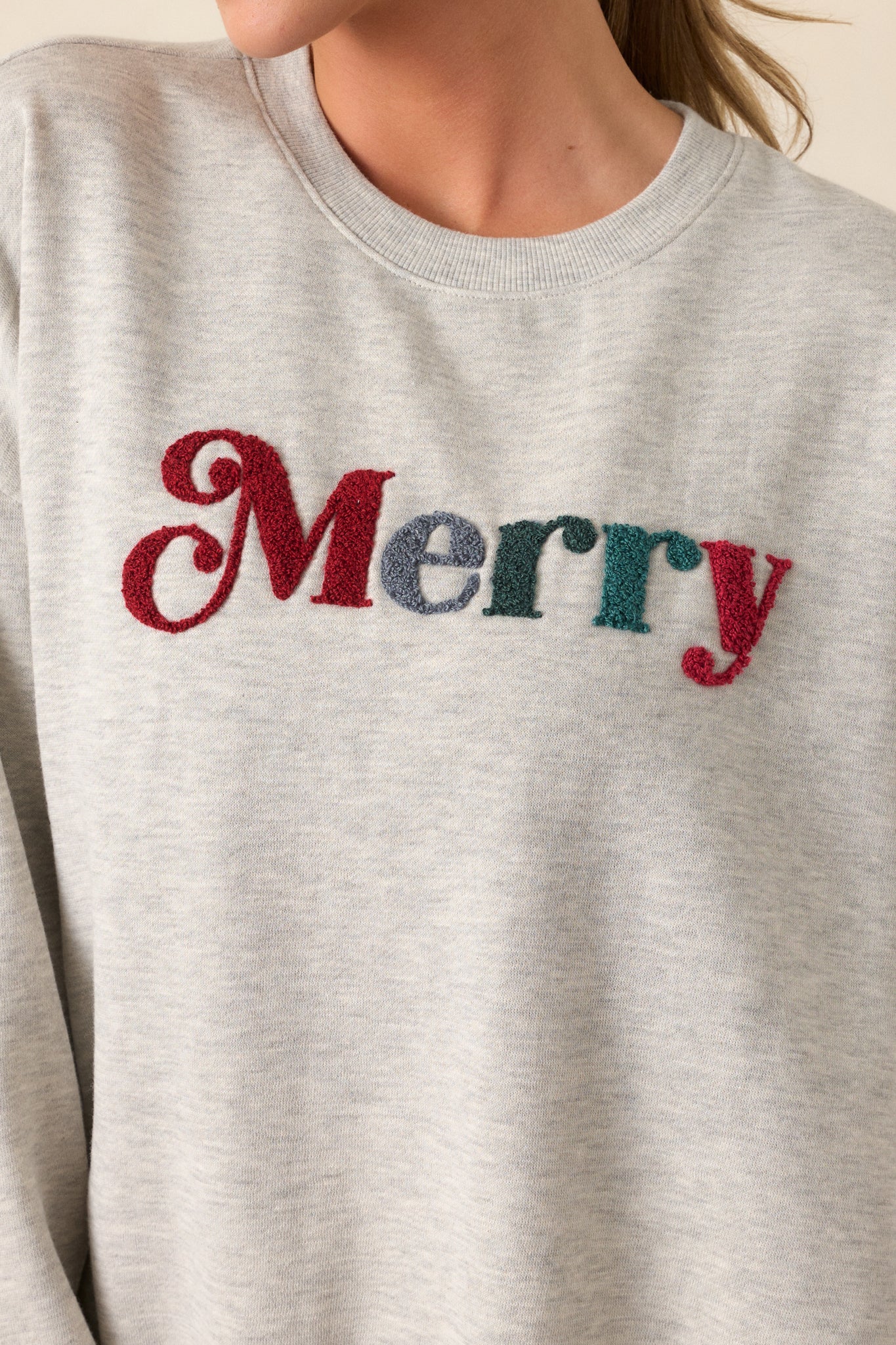 A detailed shot of the "Merry" graphic on the chest, emphasizing the festive text with a soft contrast against the light heather grey fabric.