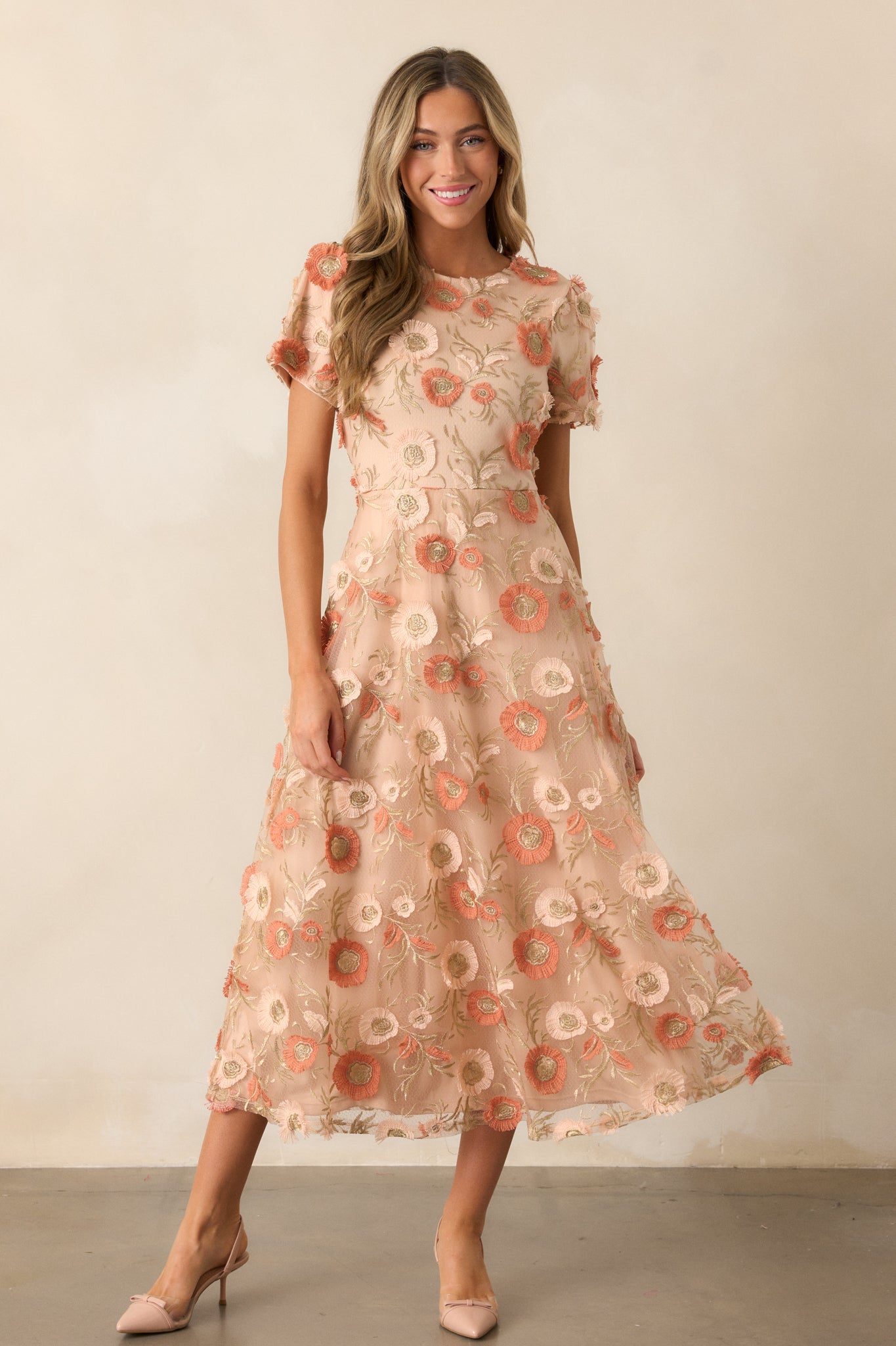 Front view of the tan dress highlighting the round neckline, embroidered floral overlay, and the graceful flow of the fit-and-flare skirt as it extends from the waist.