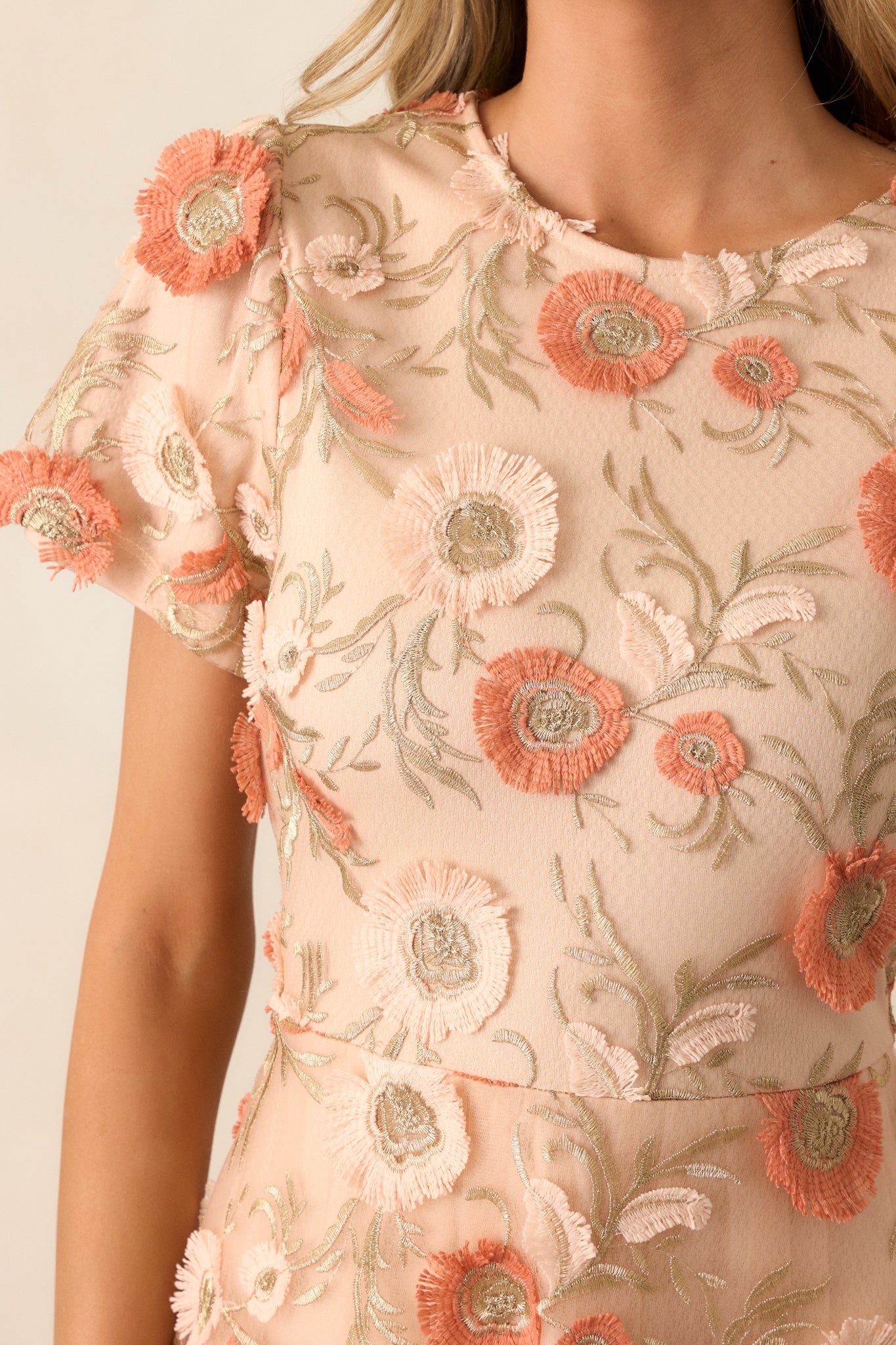 Close-up of the embroidered floral overlay on the tan dress, highlighting the intricate stitching and delicate design.