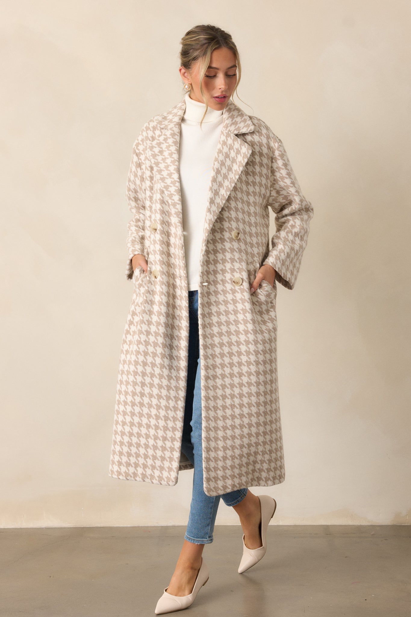 Full body view of a beige trench coat with a lapel neckline, houndstooth print, and midi length. The coat is unbuttoned, showing its functional pockets and long sleeves.