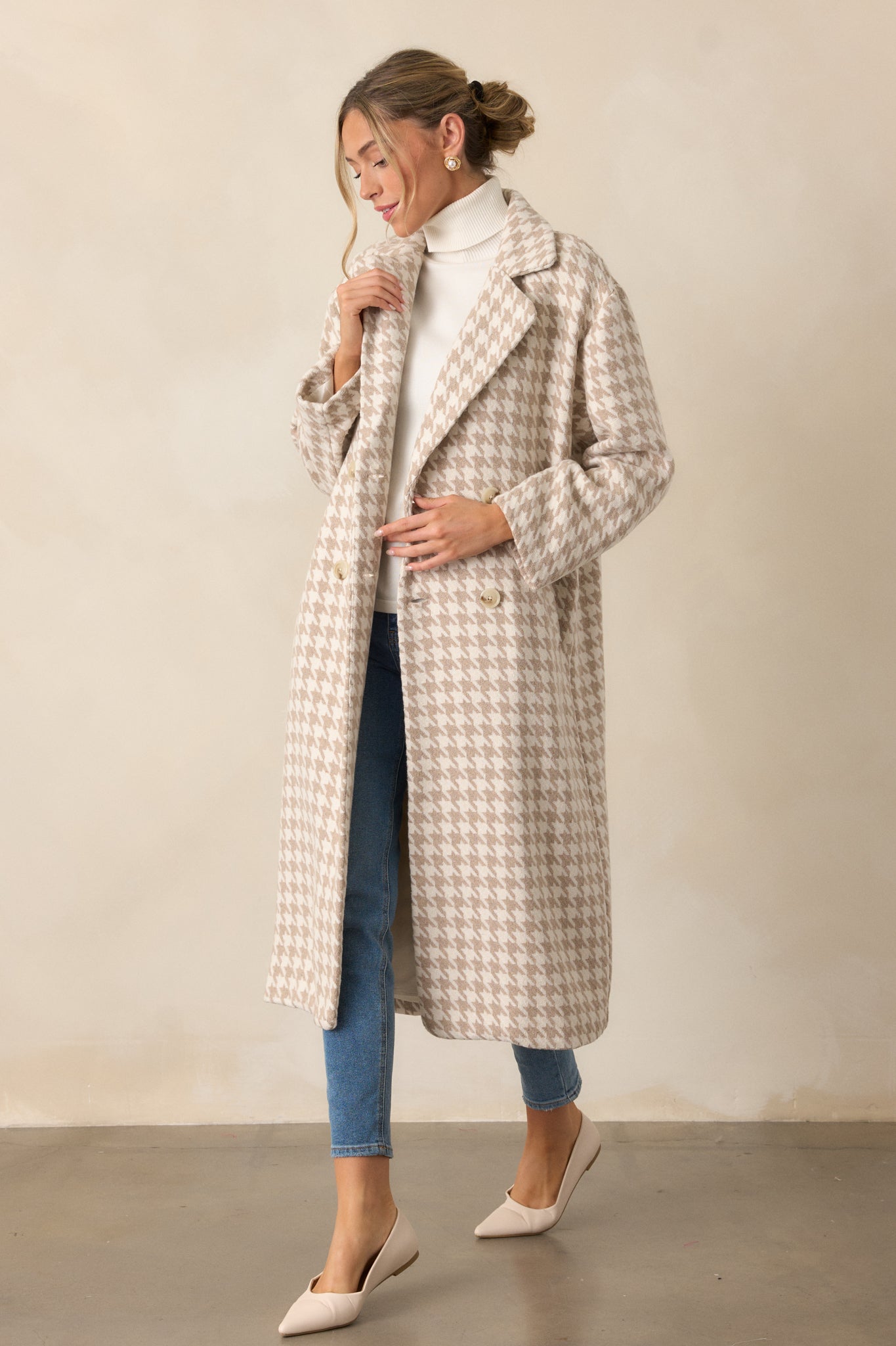 Angled view of the beige trench coat with its houndstooth print, button front, and lapel neckline. The midi length and long sleeves give it a sophisticated style.