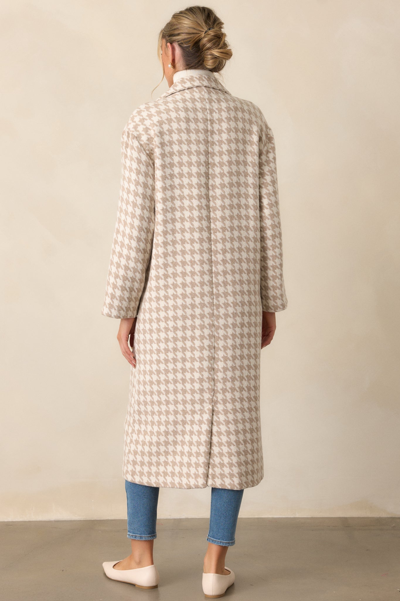 Back view of the beige trench coat showing its houndstooth print, long sleeves, and midi length. The clean lines and tailored design are visible from this angle.