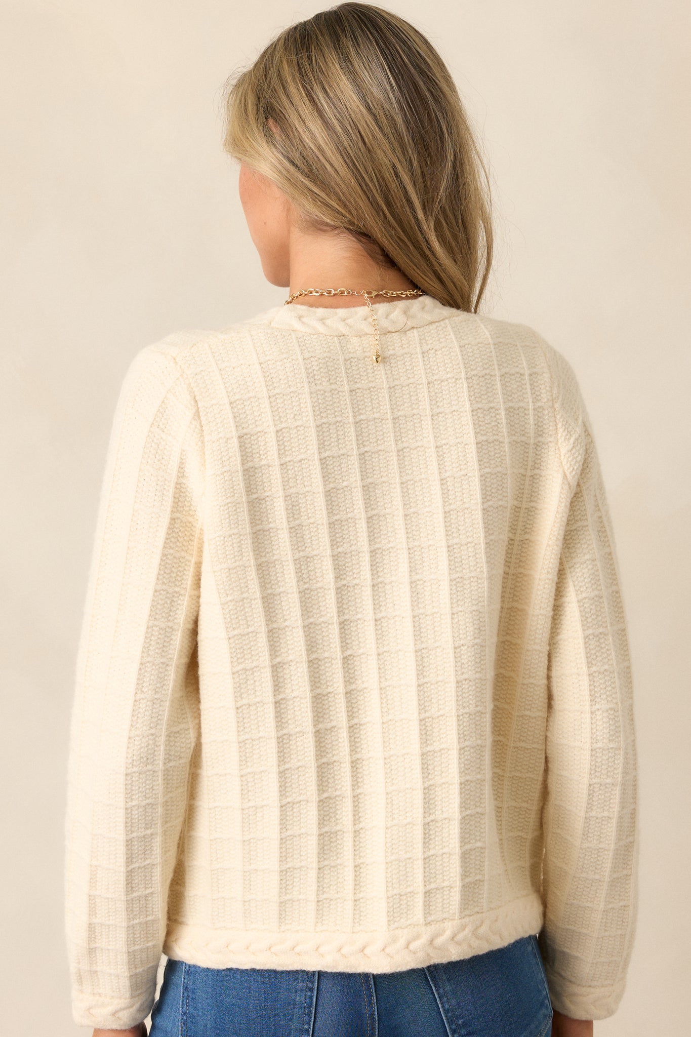 A back view of the ivory cardigan, showing the continuation of the cable knit grid design and the clean, structured fit of the long sleeves and hemline.