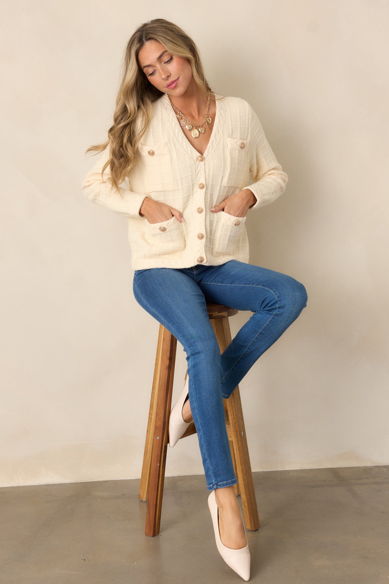 A full view of the ivory cardigan with focus on the elegant gold buttons and long sleeves. The braided knit detailing along the hemline adds a subtle accent.