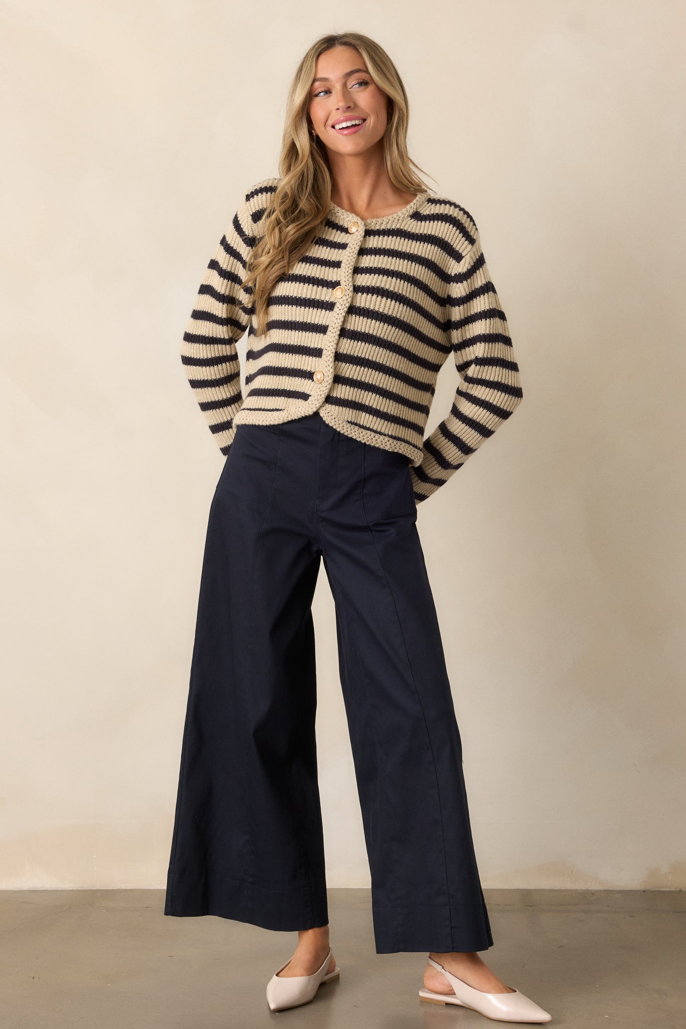 A full-length shot of a tan cardigan with black and tan stripes. The cardigan has a rounded neckline with intricate braided knit detailing, a button front with gold embellished buttons, and long sleeves for a cozy and fashionable look.