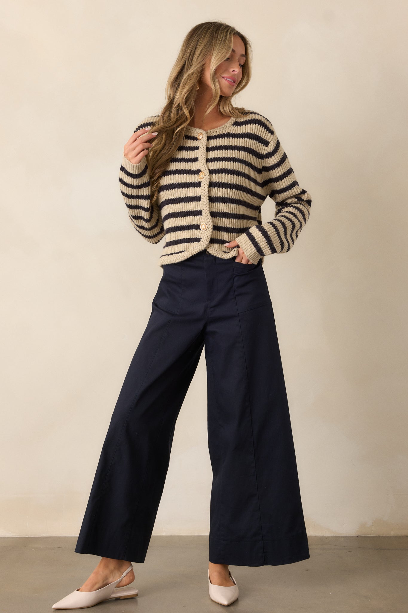 Full view of navy pants with a high waist, featuring a button and zipper closure at the front. The pants have a wide-leg fit, and the rectangular hip pockets are visible on each side, adding to the modern, clean lines