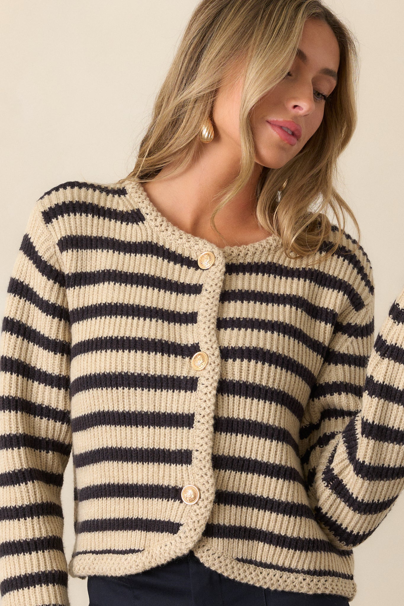 A cropped shot of the tan cardigan highlighting the black and tan stripe pattern. The rounded neckline with braided knit detailing and the gold embellished buttons on the front are clearly visible.