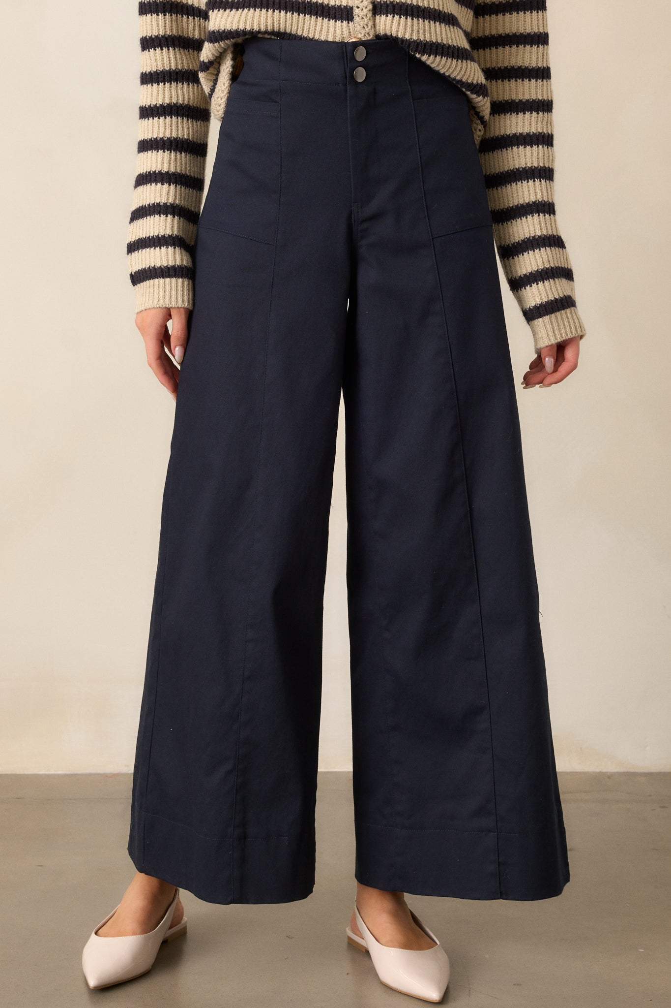 A closer look at the navy pants, highlighting the wide-leg cut and the button and zipper closure at the front. The rectangular hip pockets are visible, adding a casual yet functional element to the design.