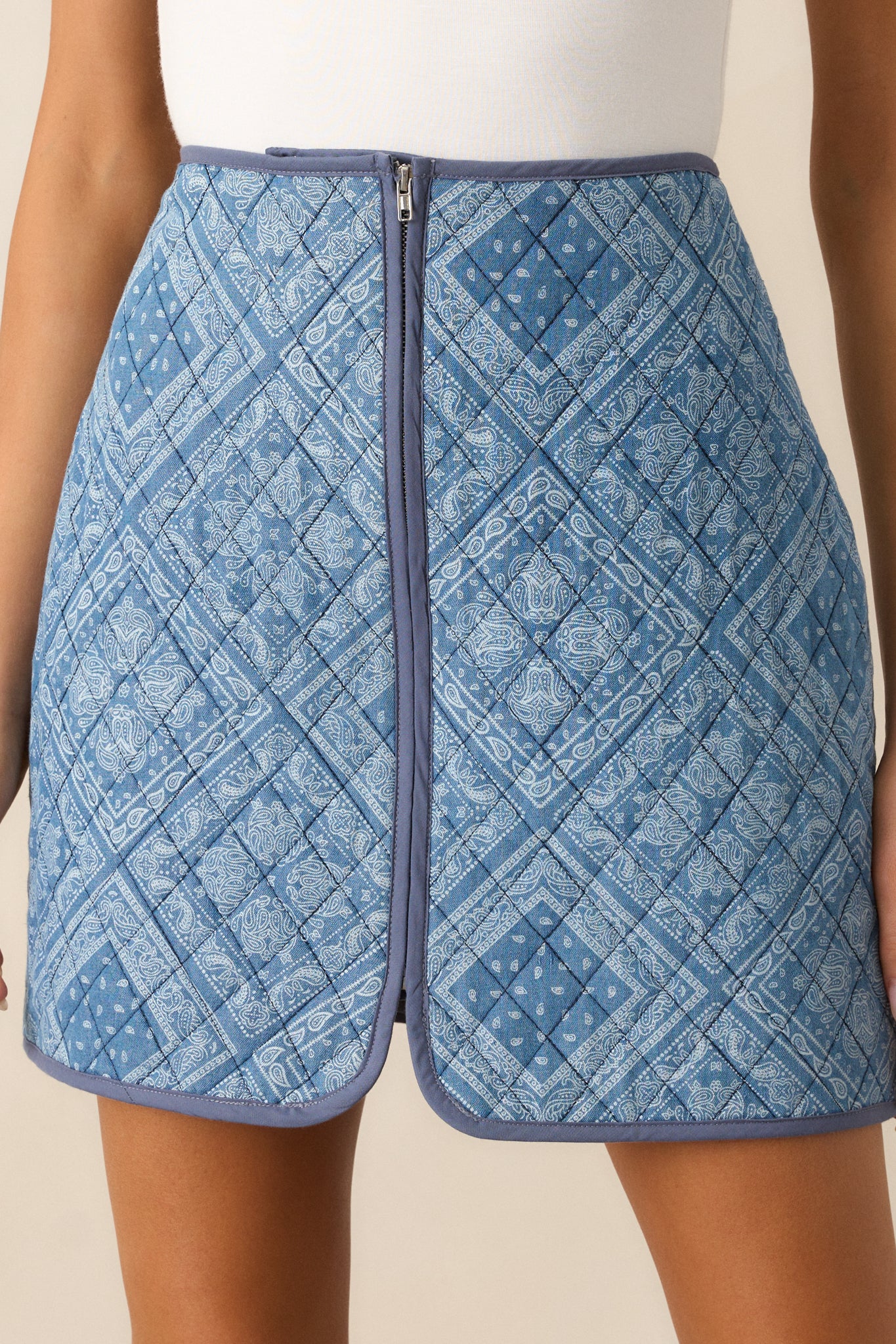 A close-up of the light blue mini skirt’s high waist and quilted design, with a functional zip front. The navy trim and geometric paisley print are visible, creating a striking contrast and adding dimension to the overall look.