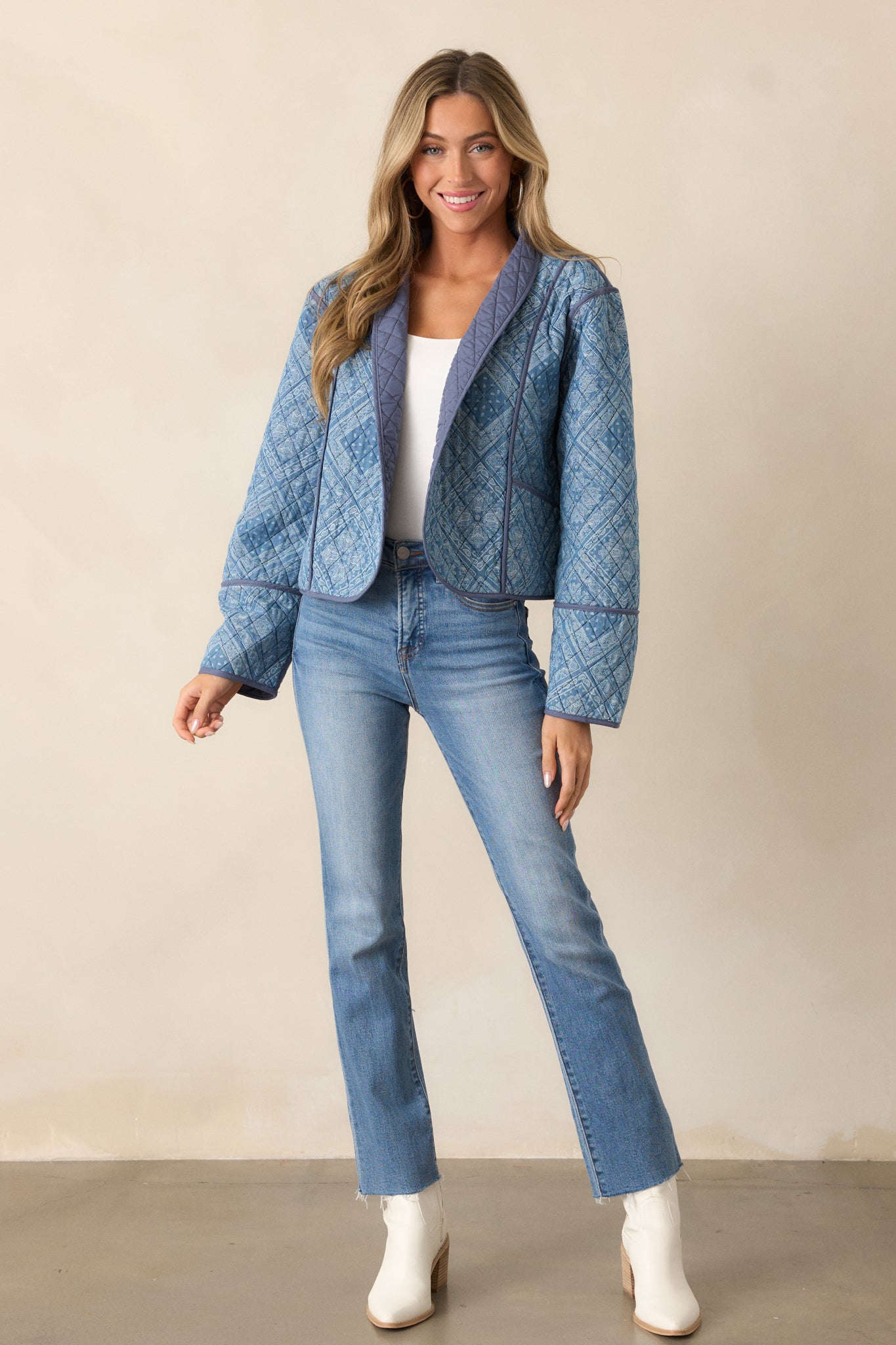 Full-body view of a light blue jacket with shawl lapels and a quilted design. The jacket features navy trim detailing along the edges and functional pockets. The geometric paisley print adds a unique touch, and the long sleeves complete the look.