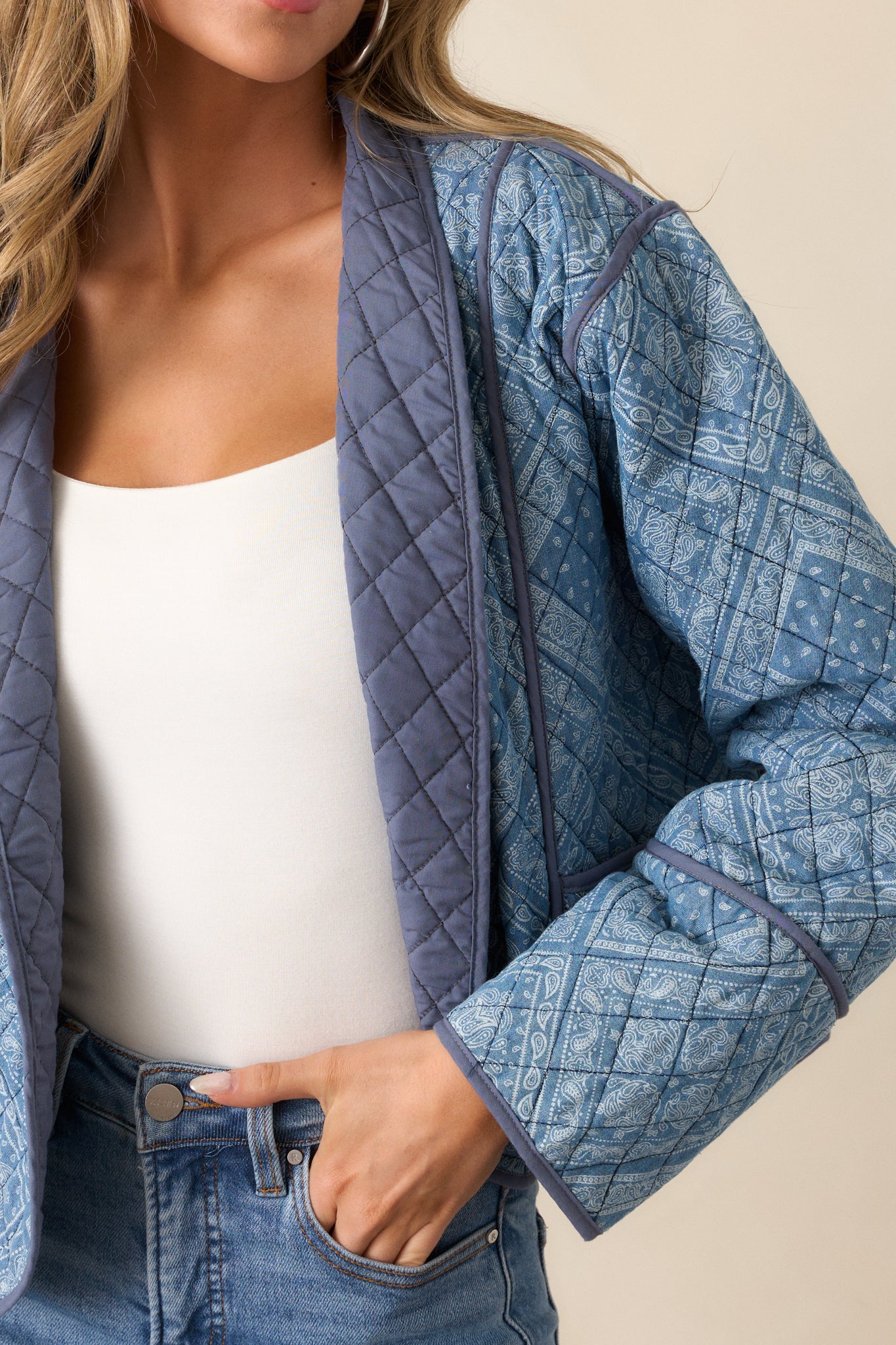 A detailed shot of the light blue jacket’s quilted design, with the shawl lapels in focus. The navy trim outlining the edges and the geometric paisley print across the fabric are clearly visible.