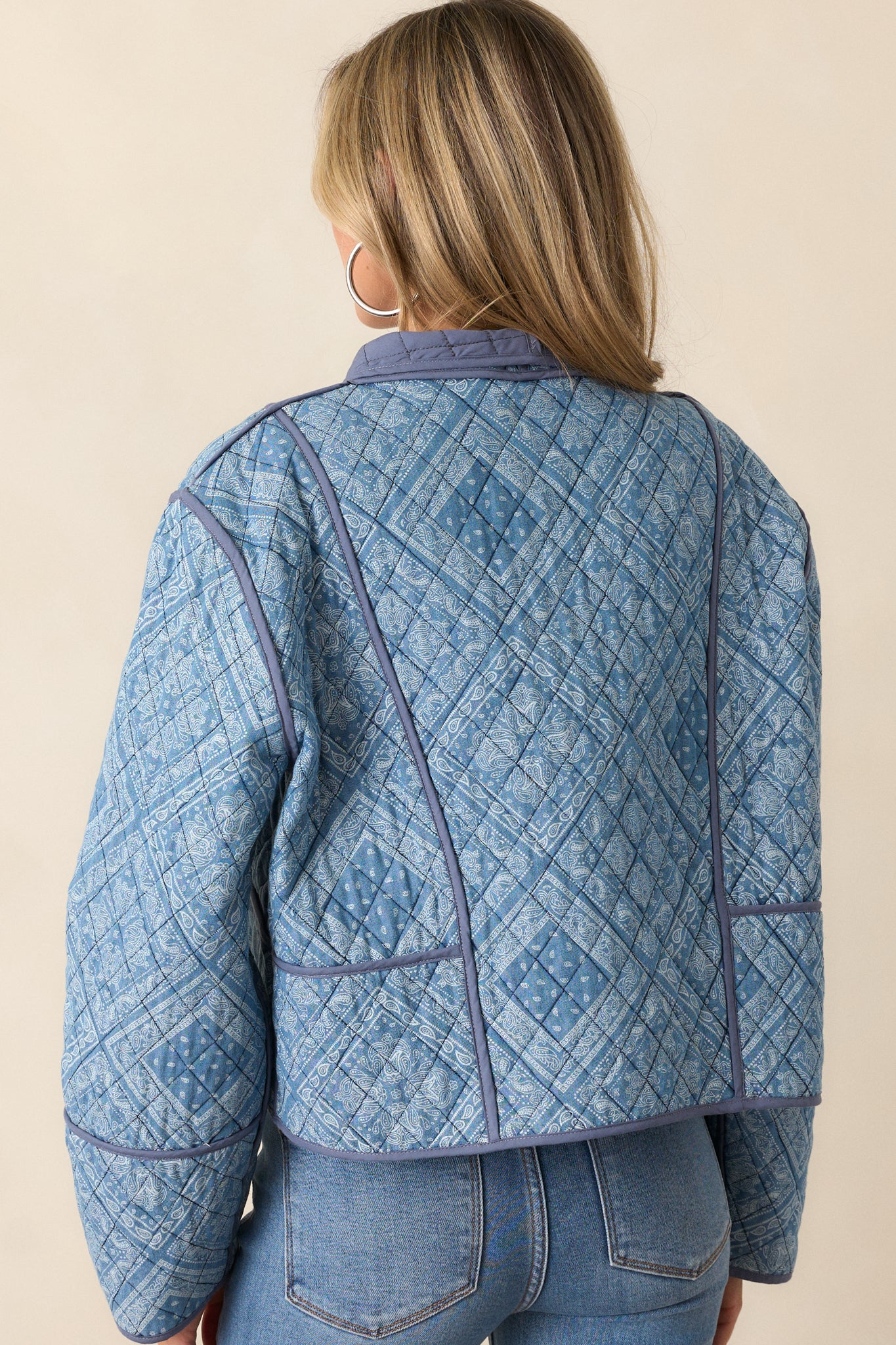 The back view of the light blue jacket with a quilted pattern and visible navy trim detailing. The shawl lapels curve around the shoulders, and the geometric paisley print covers the back, with long sleeves extending down