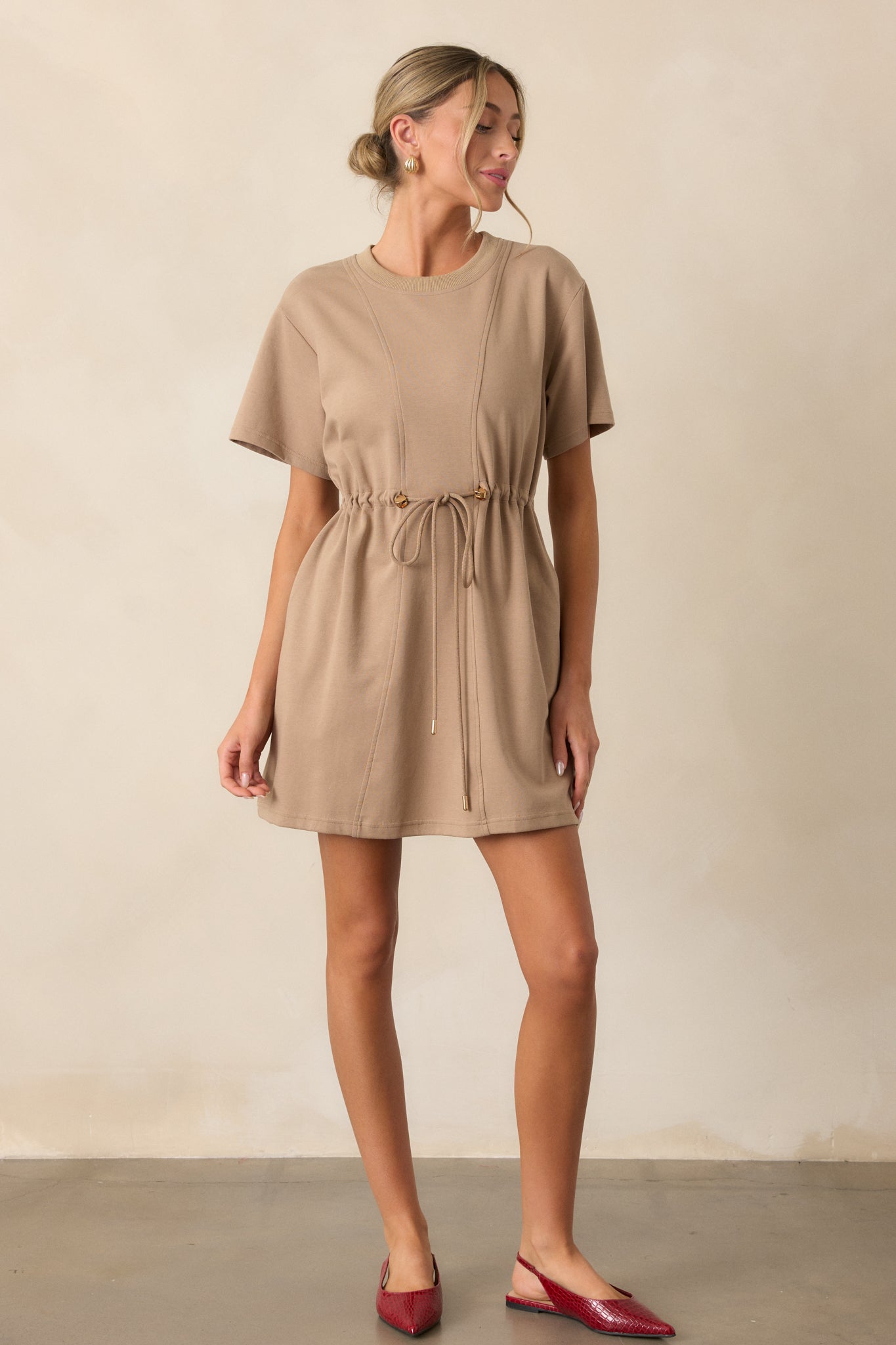 Full-body image emphasizing the flowy silhouette of the light mocha mini dress with a drawstring waist and short sleeves.