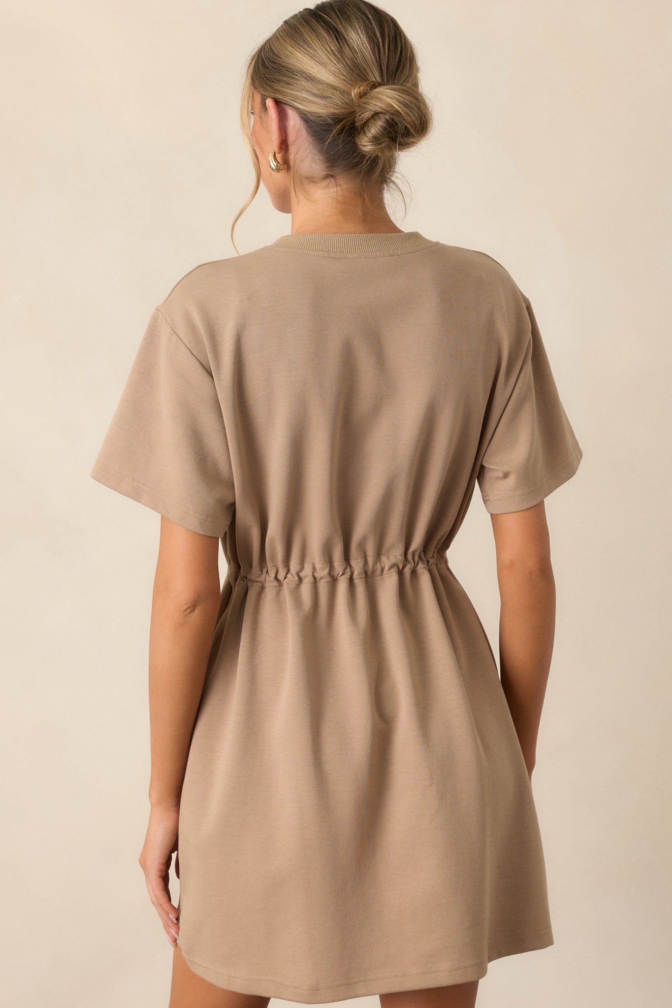 Back view of the light mocha mini dress displaying the clean lines and seamless finish with short sleeves and a soft silhouette.