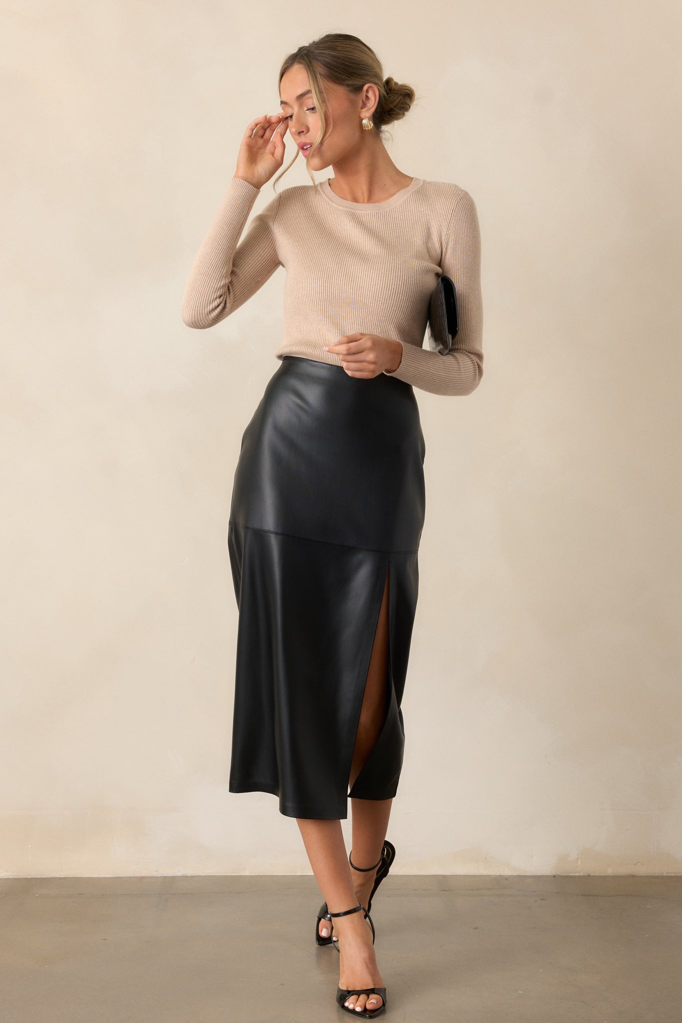 A black midi skirt featuring faux leather paneling and a sleek silhouette is displayed in a full-body side view, emphasizing the side slit.