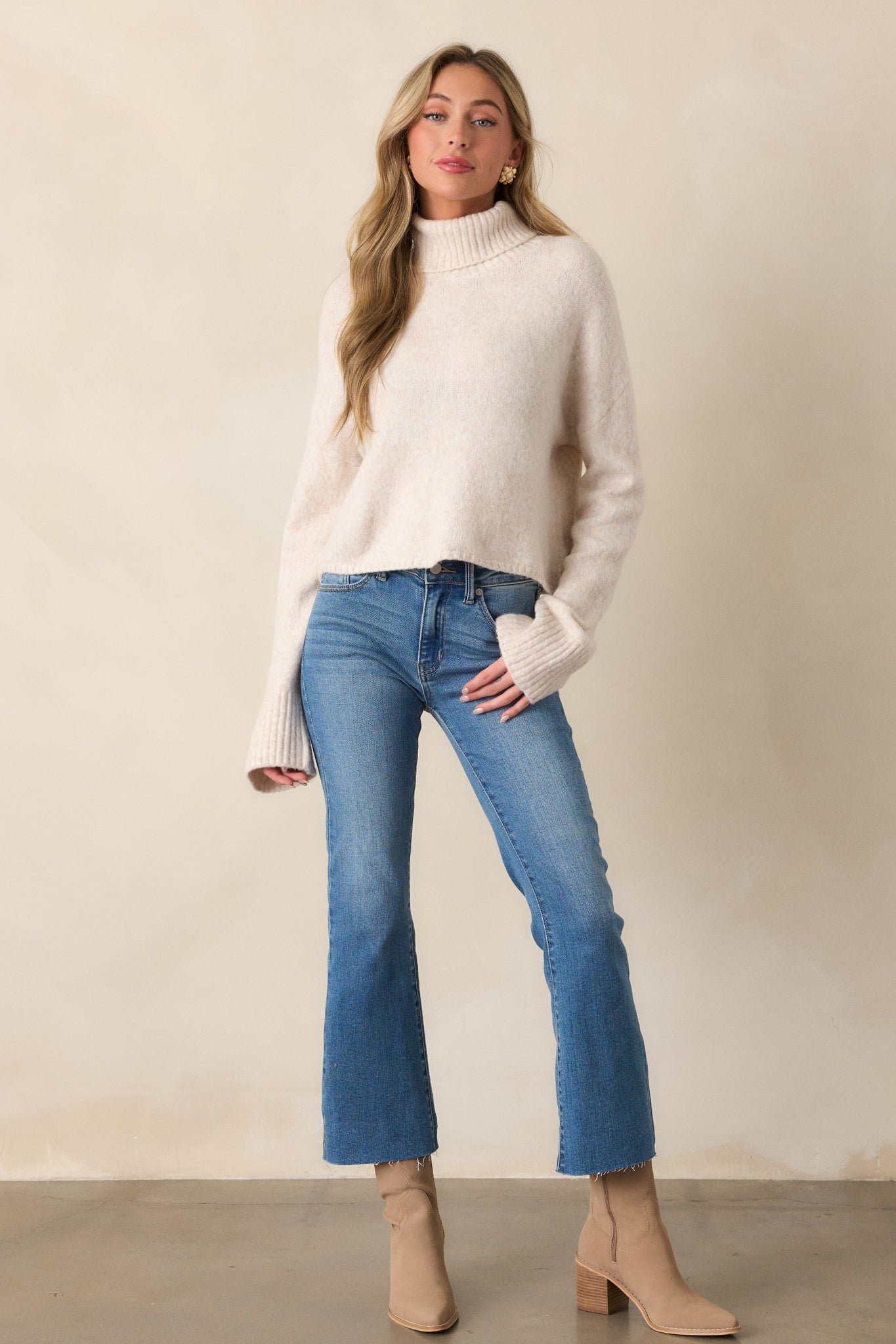 Front view of a light oatmeal sweater featuring a ribbed turtleneck, long sleeves with thick ribbed cuffs, and a relaxed fit with a ribbed bottom hem.