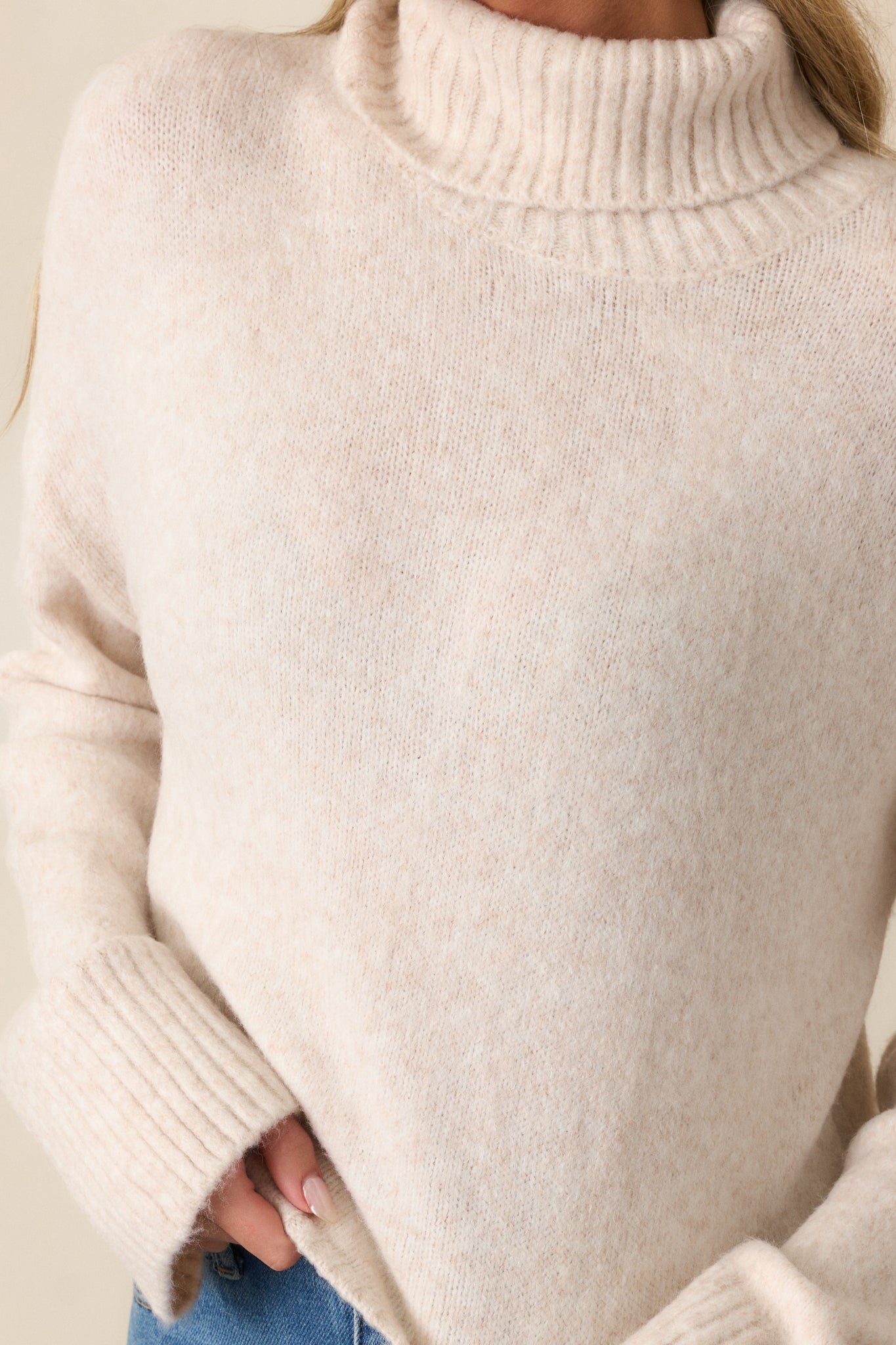 Extreme close-up of the ribbed turtleneck of the light oatmeal sweater, showcasing the intricate knit pattern and soft texture.