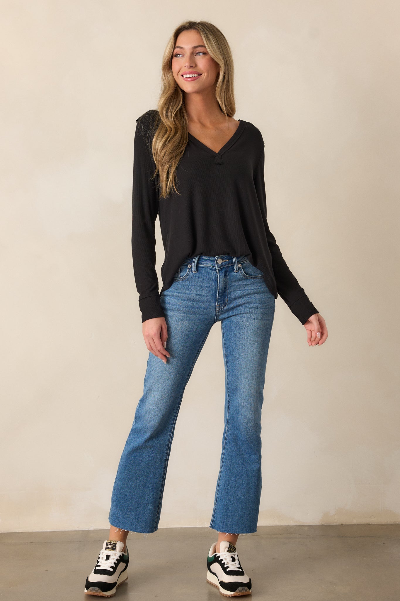 Front view of a black top featuring a V-neckline, long sleeves, and a soft ribbed design with a curved bottom hem.