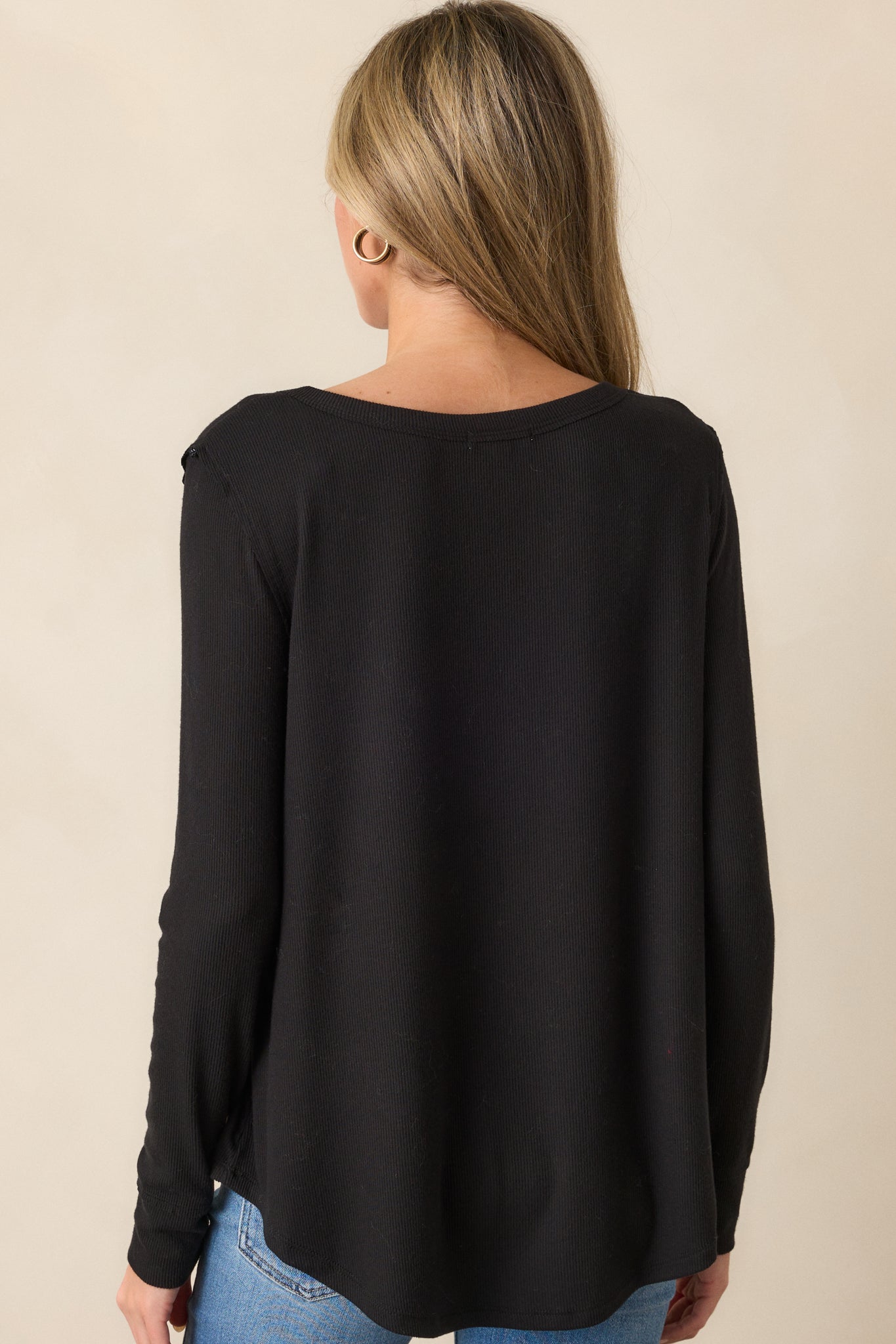 Back view of the black top, highlighting the soft ribbed texture, long sleeves, and curved bottom hem that create a flattering fit.