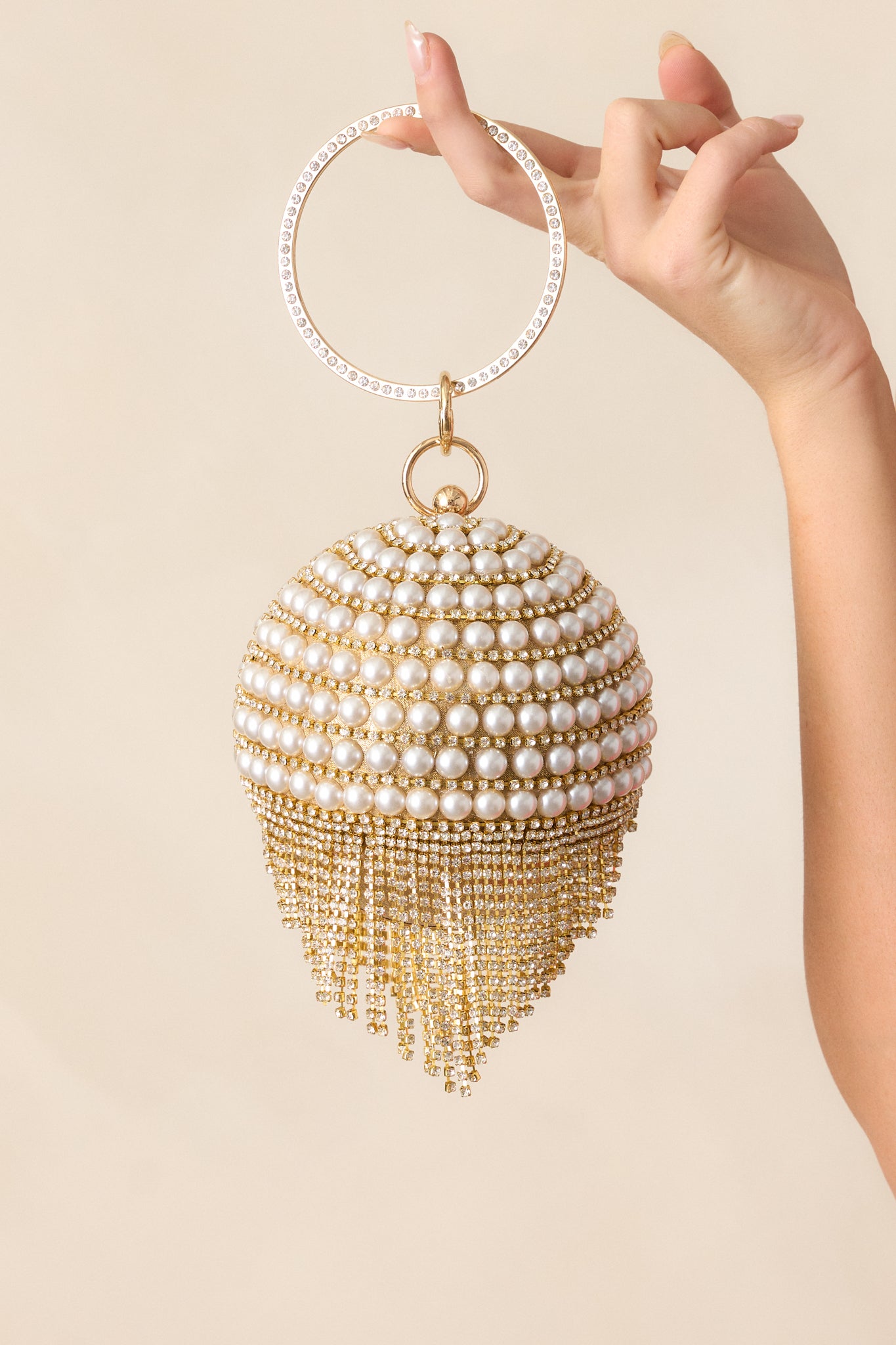 The gold and ivory clutch from the front, highlighting the dangling diamond accents and gold closure against the pearl-encrusted design.